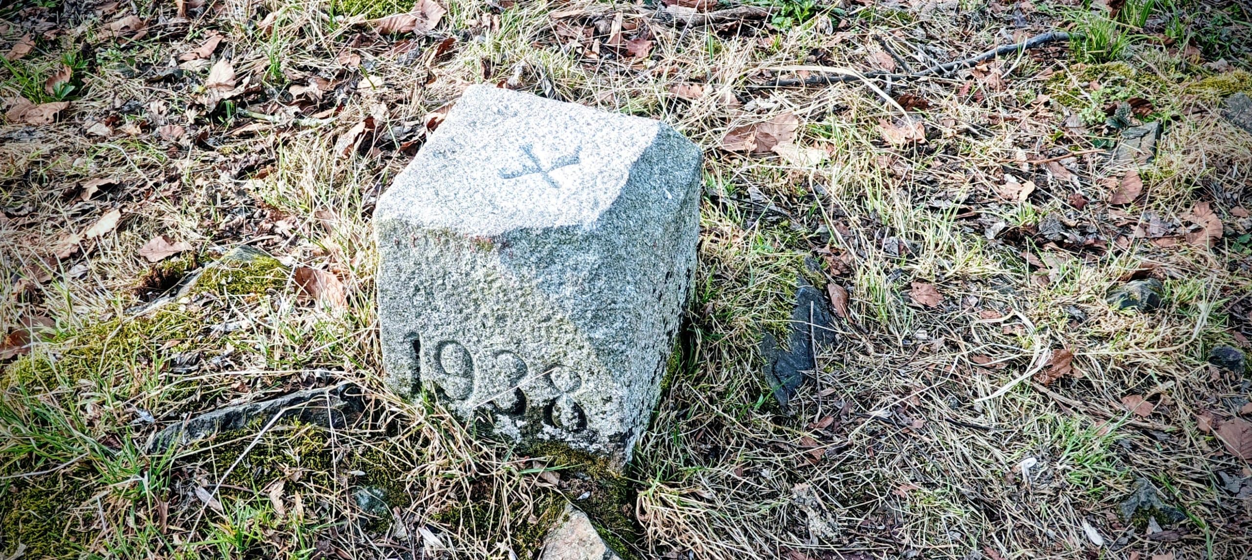Square concrete survey block marked 1938 beside grass, leaves and moss near the Běleč summit.