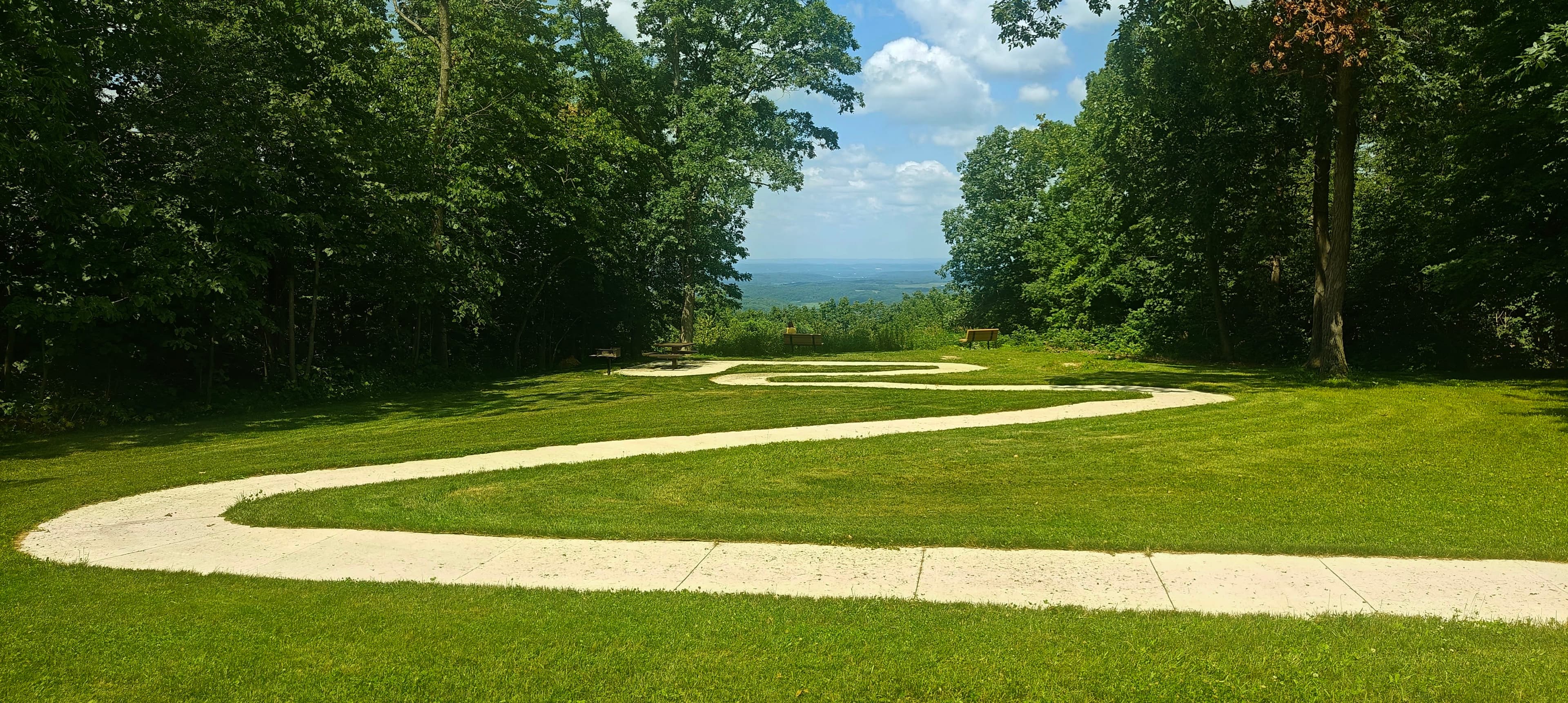 Curving paved paths crossing a mown lawn between trees near the Blue Mound summit area.