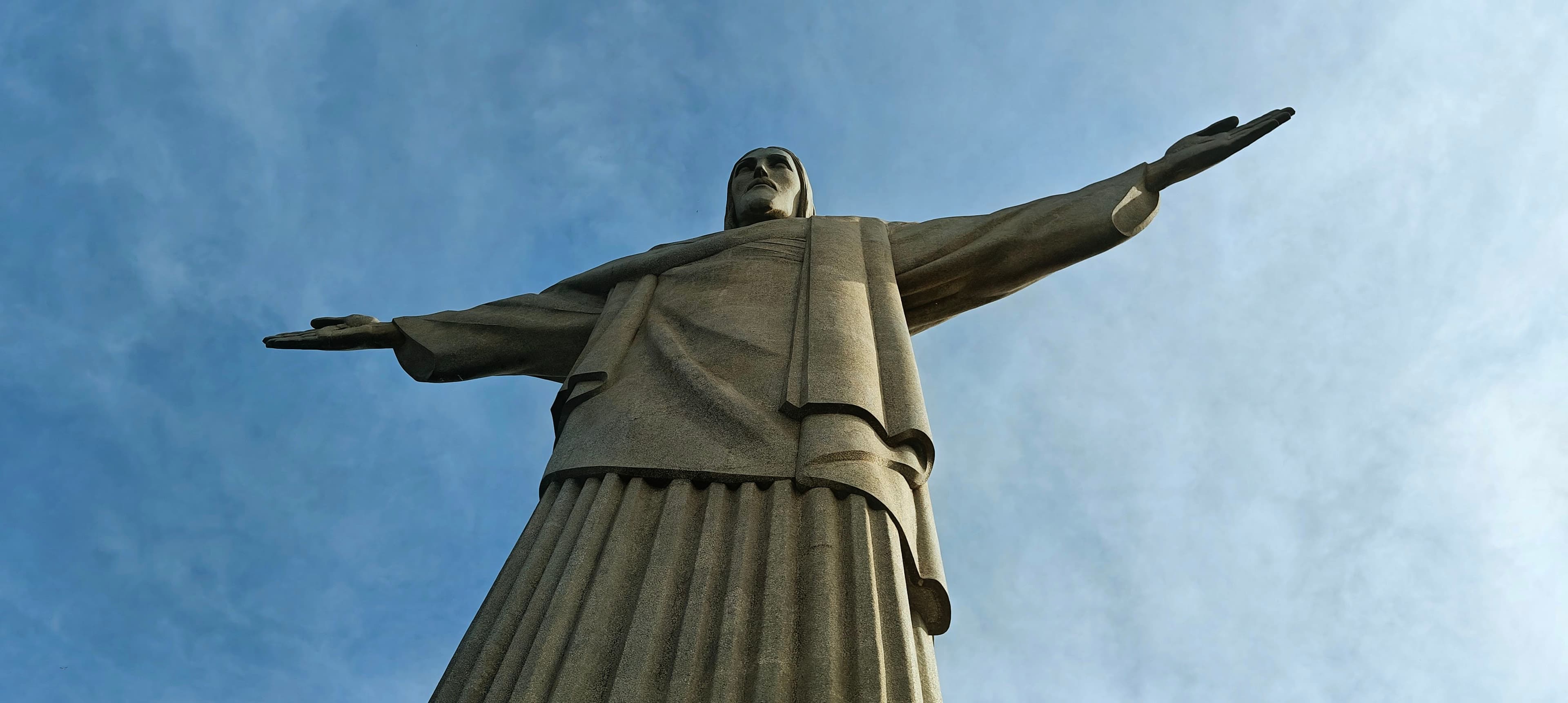 Christ the Redeemer photographed from below, its outstretched arms silhouetted against blue sky.