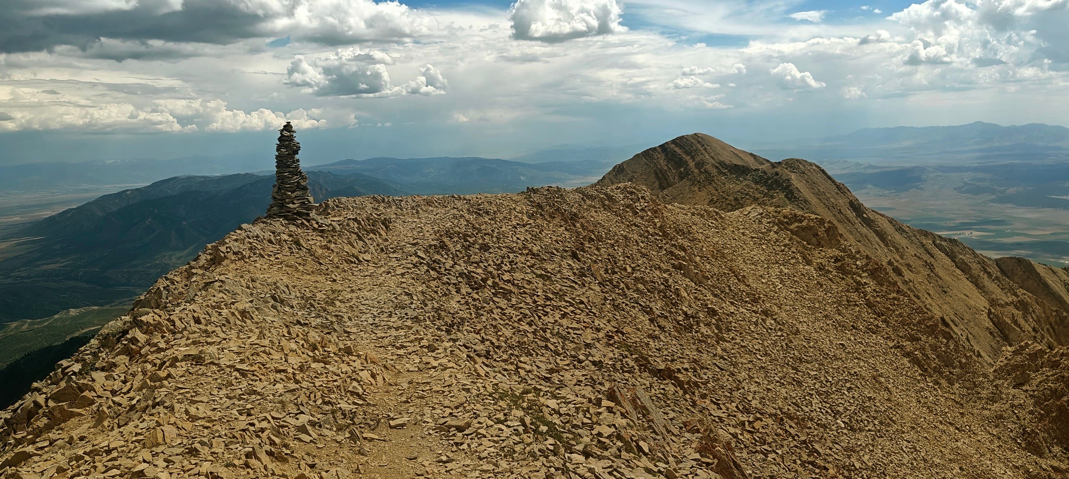 A small stone cairn on an exposed rocky mountain ridge with higher ground beyond.