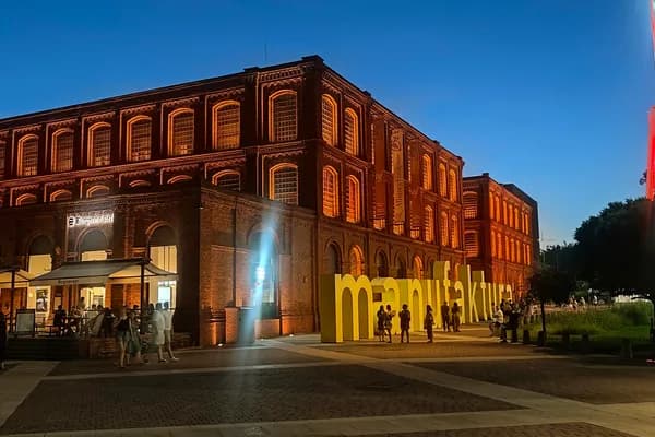 Illuminated red-brick Manufaktura building at blue hour with yellow sign and Ferris wheel.