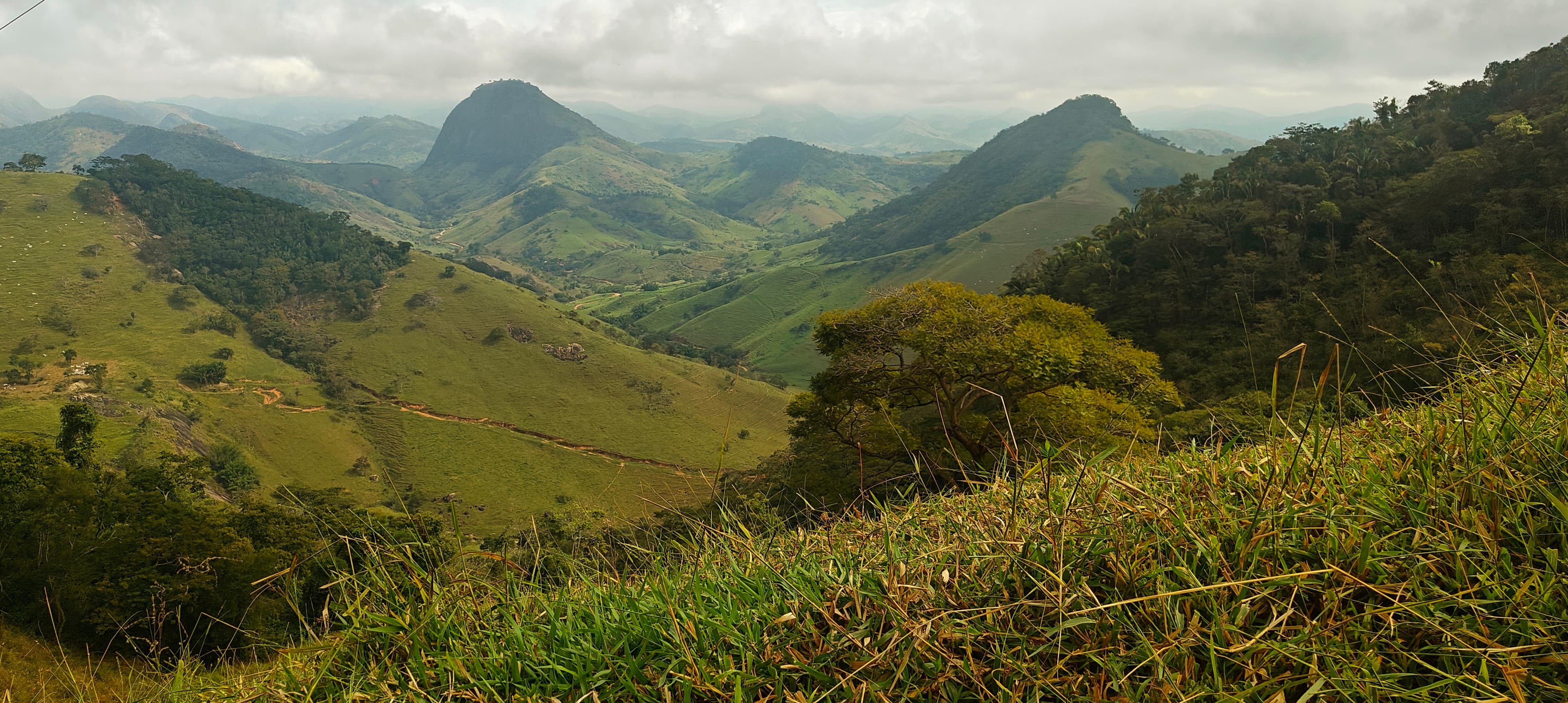 Green hills and rounded mountain ridges seen from the lower approach under broken cloud.