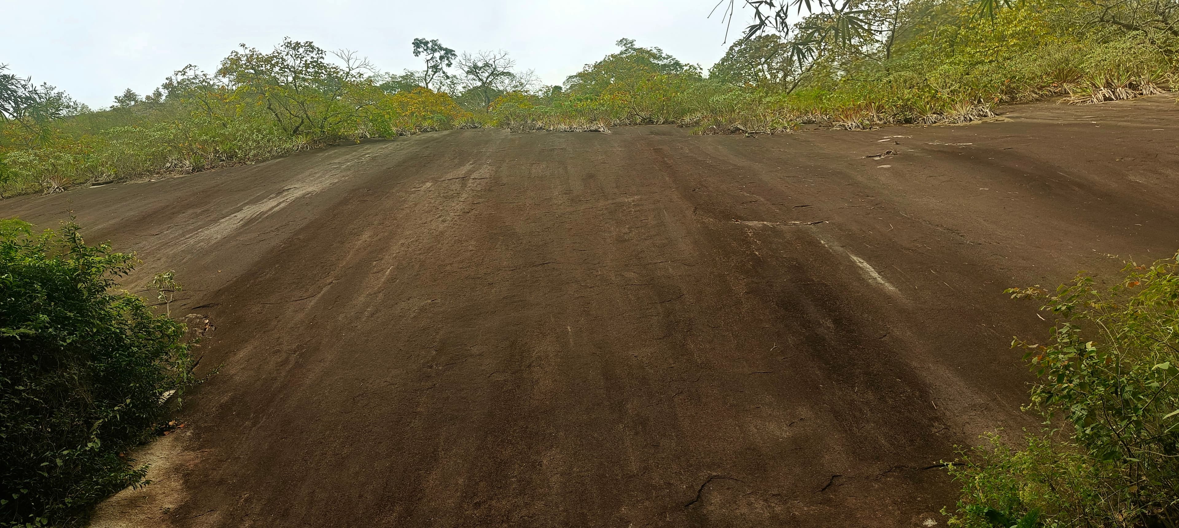 A broad steep rock slab rising immediately beside the unpaved approach road.