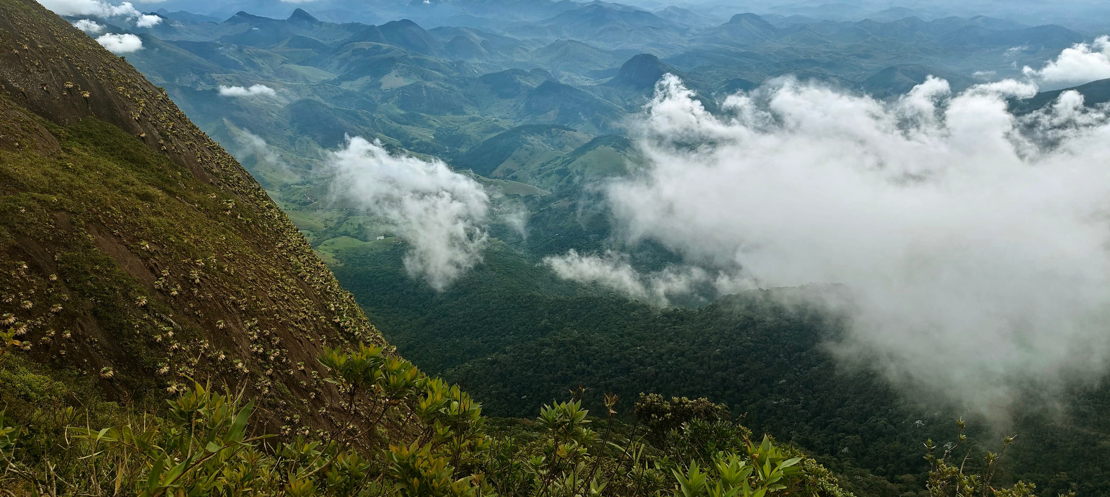 White cloud filling a deep green valley below a steep exposed mountain slope.