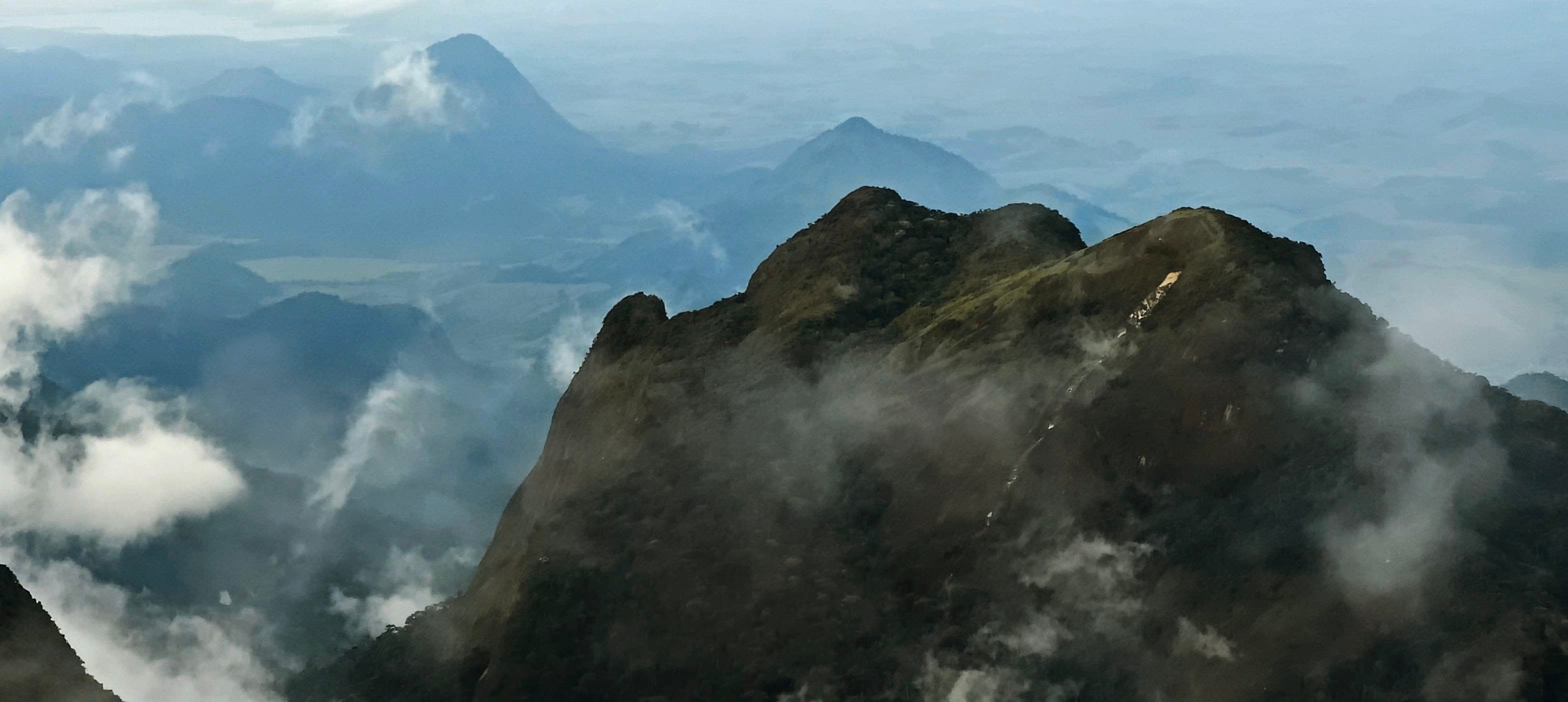 Jagged rocky ridge surrounded by low cloud and distant mountain slopes.