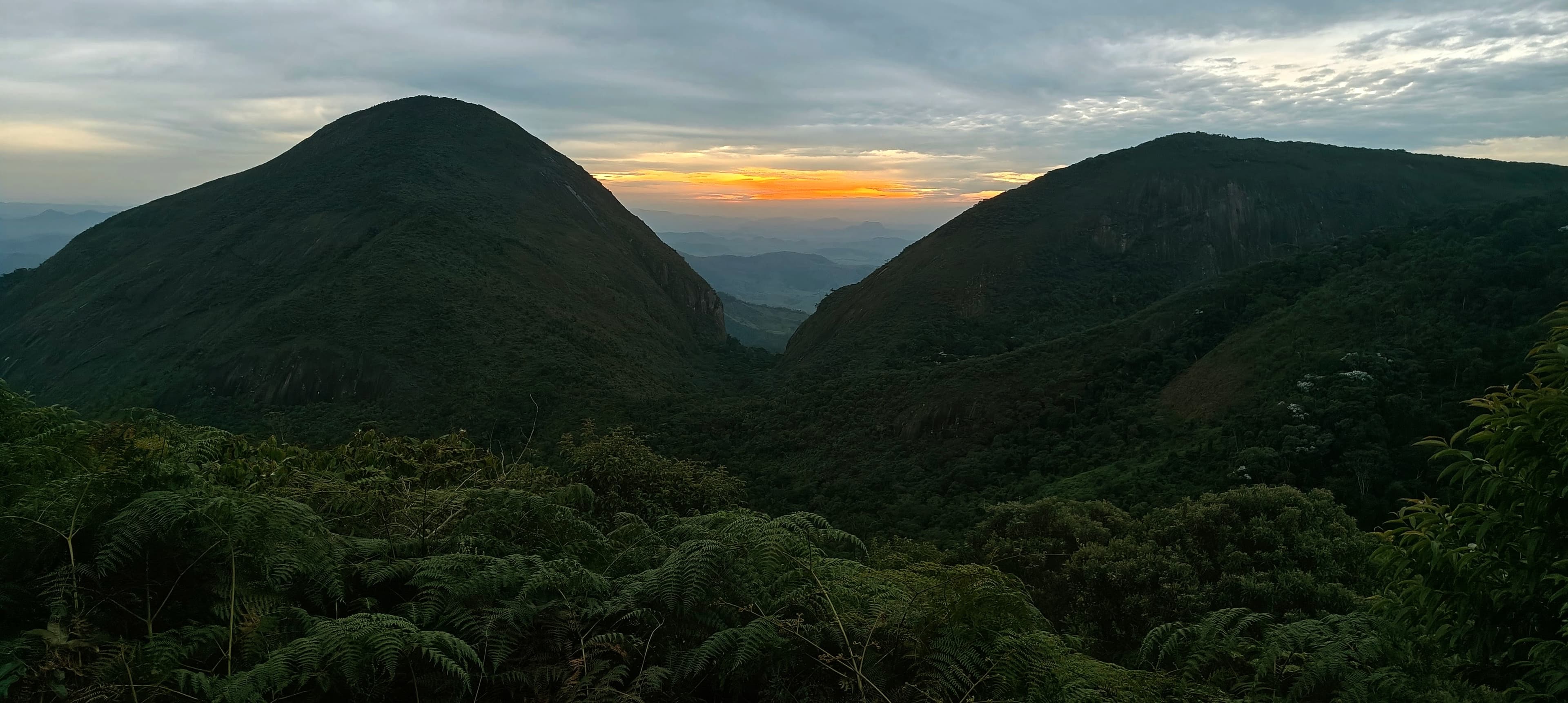 Dark forested ridges beneath a cloudy sky with a narrow band of warm evening light.