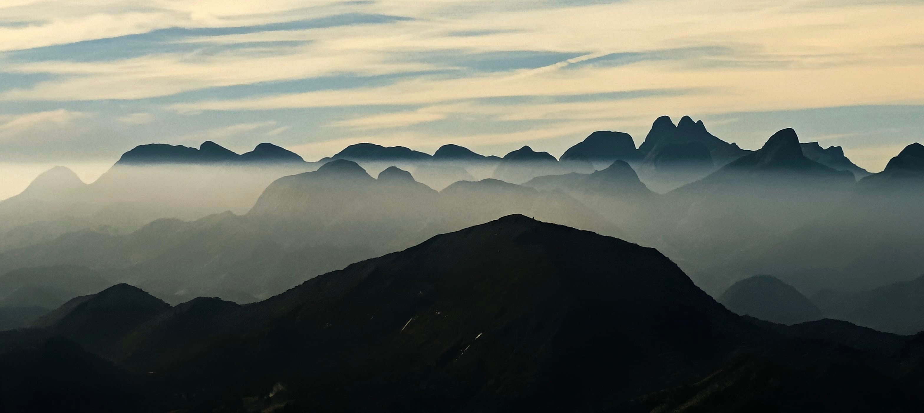 Layered mountain ridges fading into pale morning haze above a dark foreground slope.