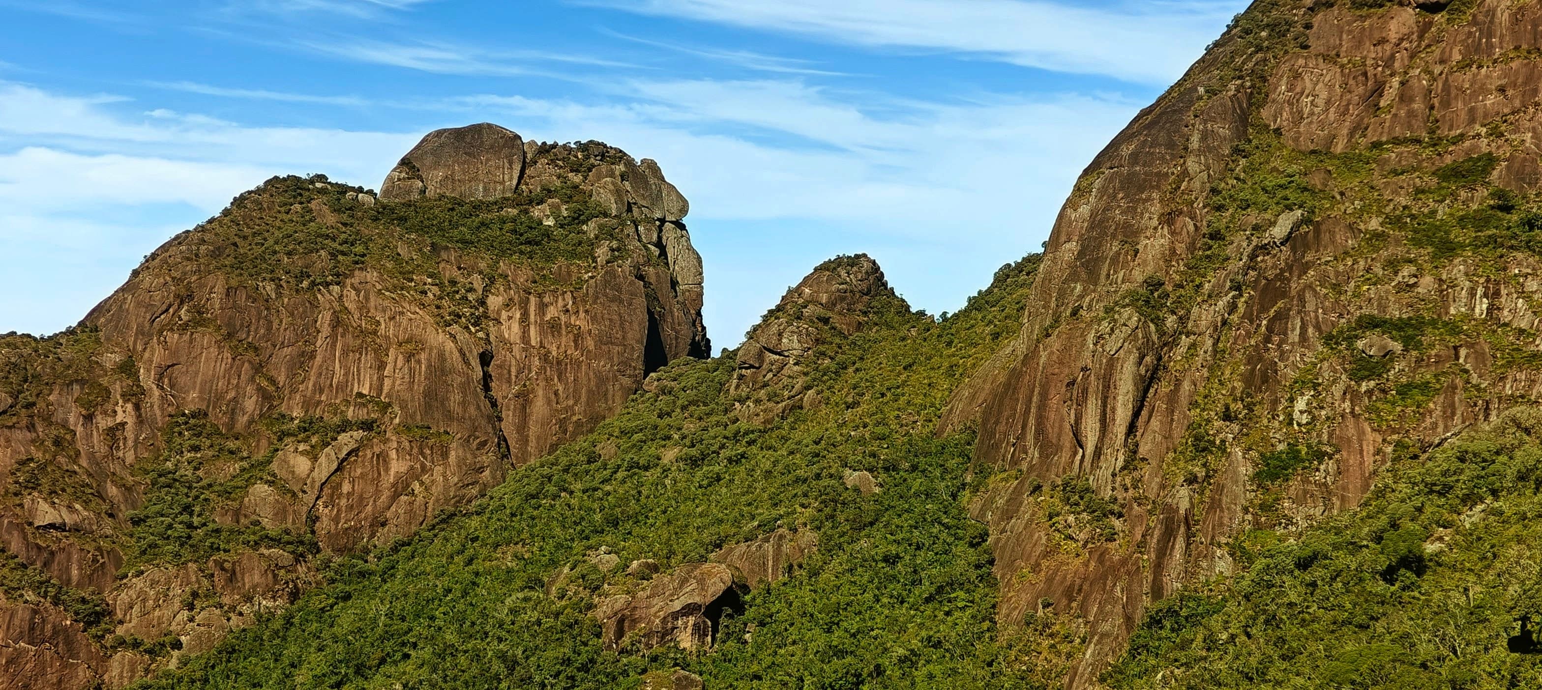 Green slopes and rounded granite cliffs under a blue sky in Serra dos Órgãos.