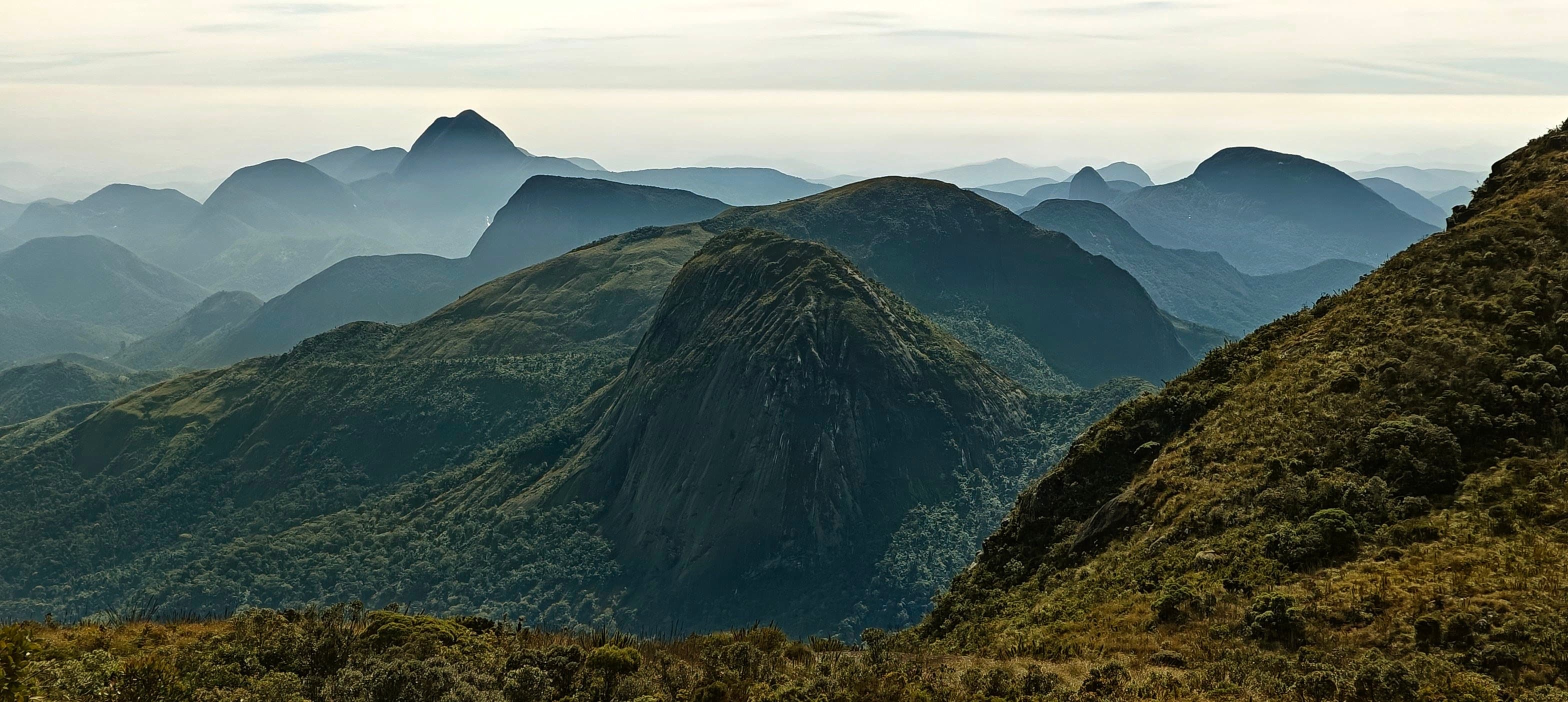 A rounded foreground ridge with pointed peaks and hazy mountain layers beyond.