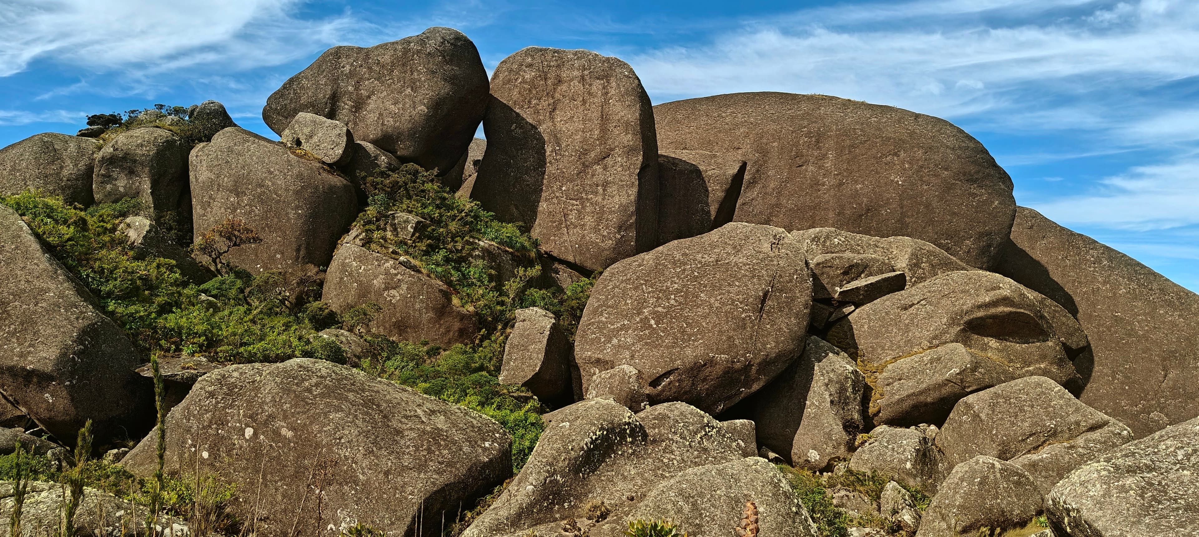 Large rounded granite boulders stacked beneath blue sky near the upper slopes of Pedra do Sino.