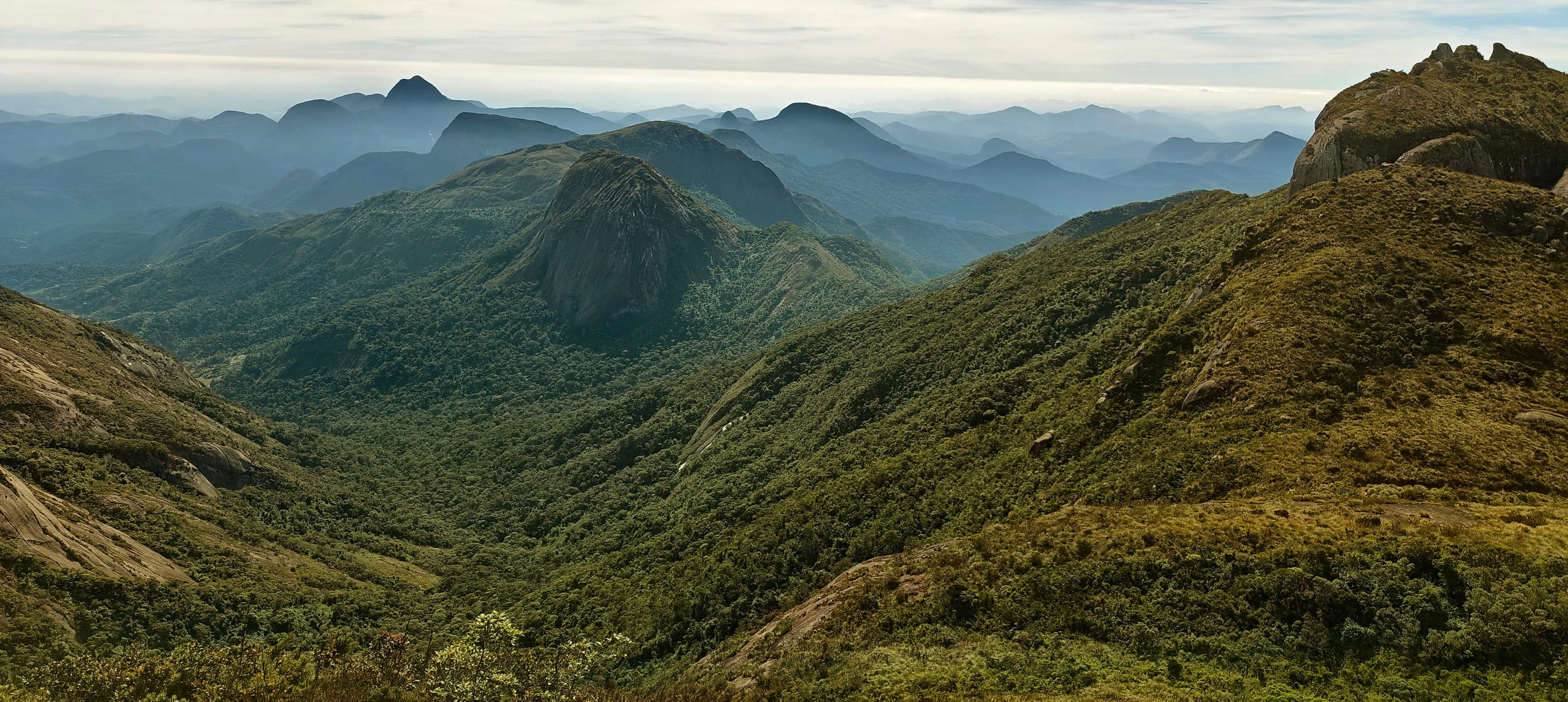 A long green valley dropping between rounded ridges with hazy peaks in the distance.