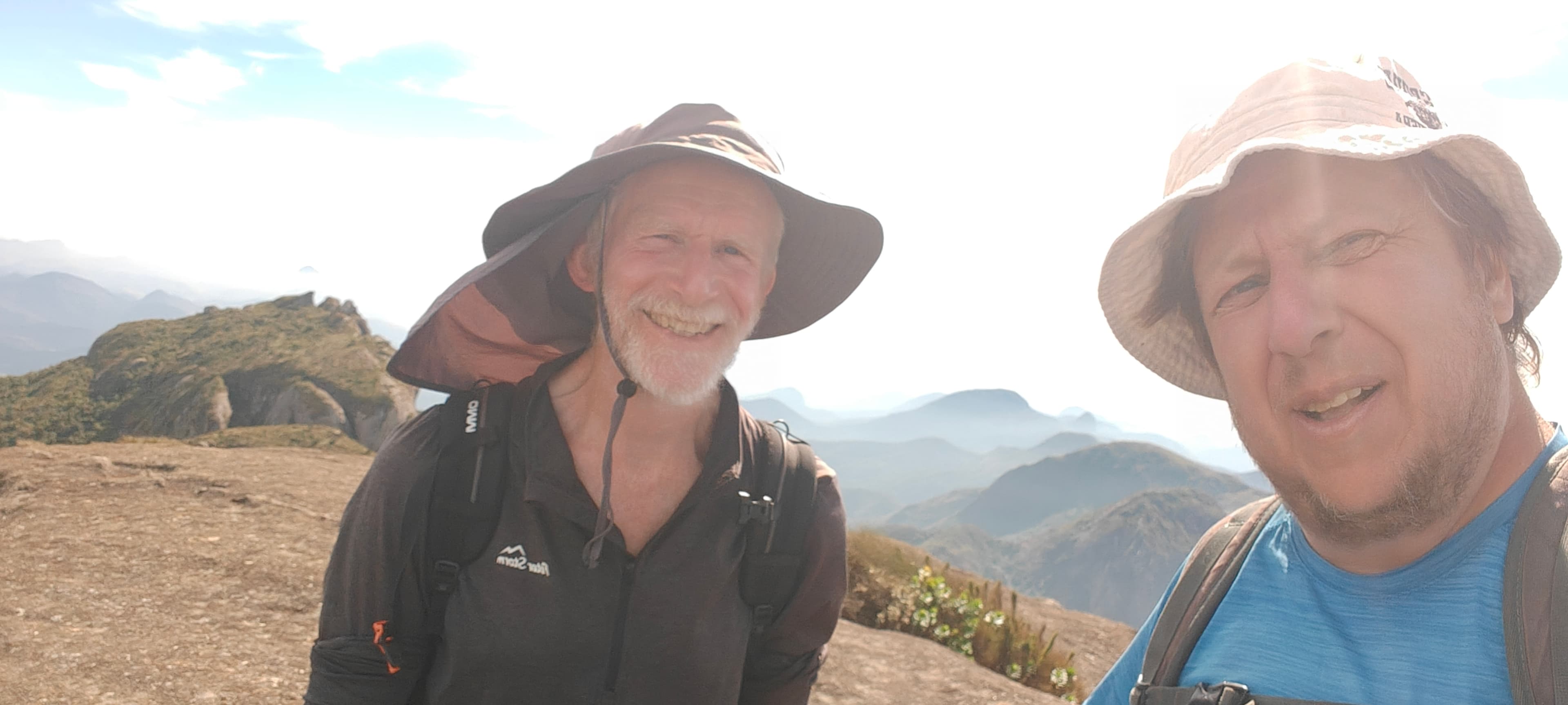Rob and Deividas smiling together on the summit area of Pedra do Sino, with Serra dos Órgãos ridges behind them.