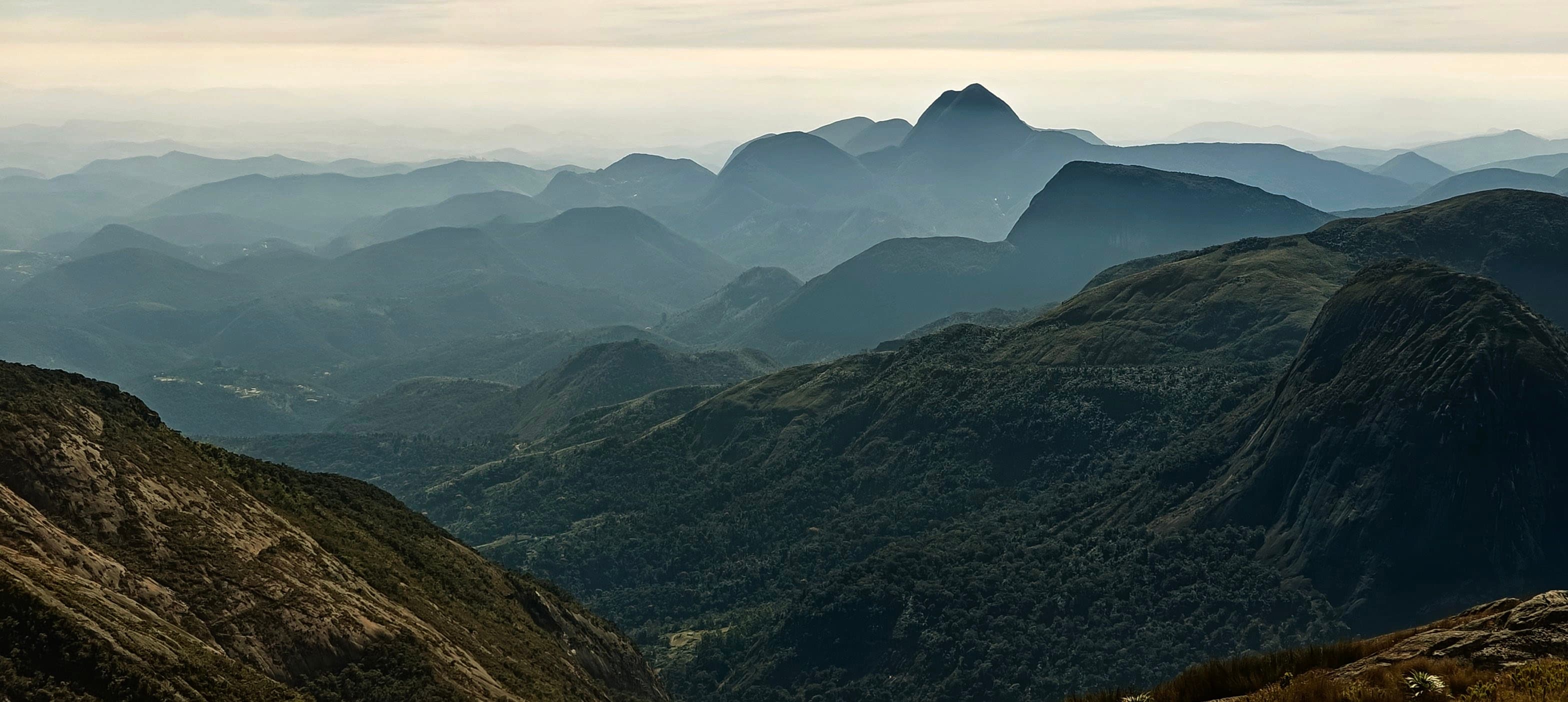 A pointed mountain peak rising above multiple dark ridges in soft haze.