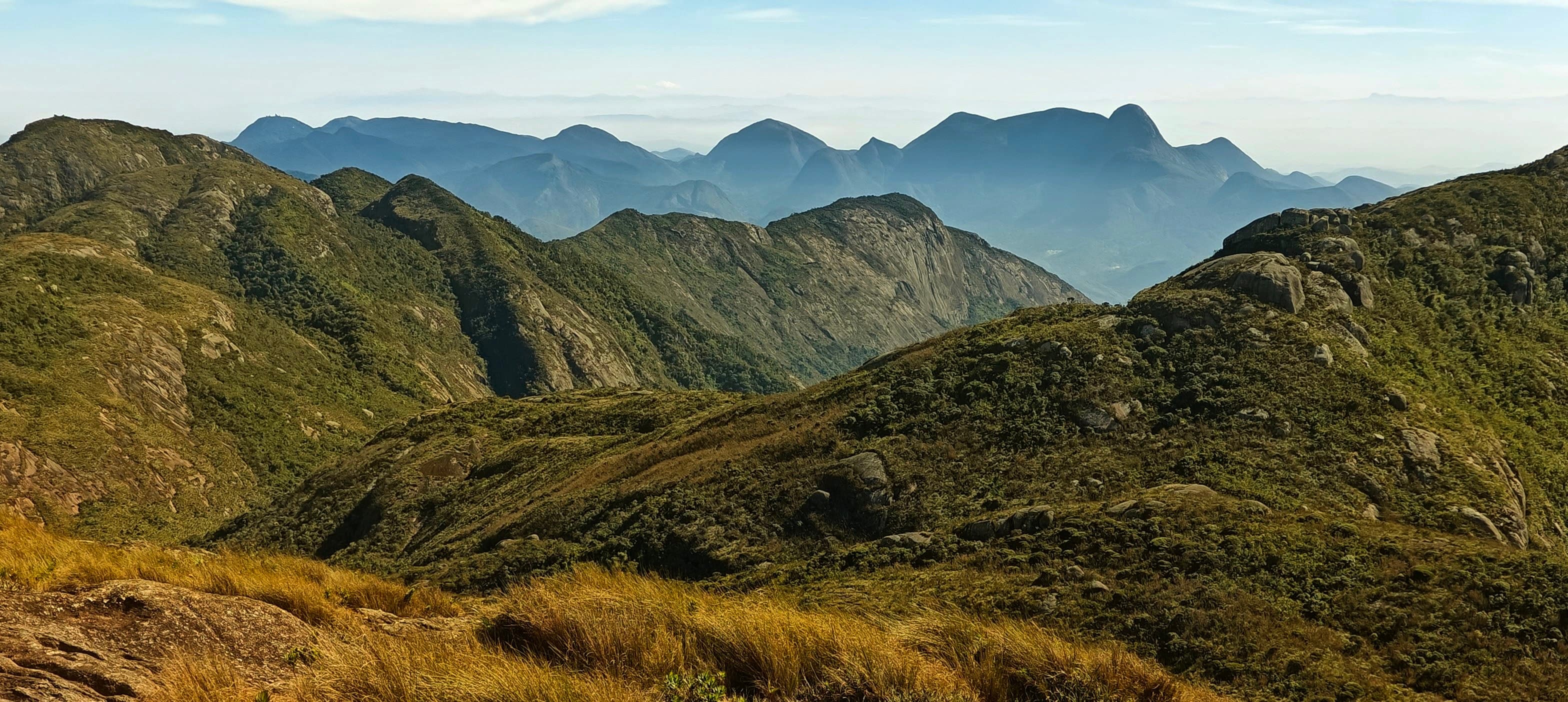 Rounded high ridges and valleys covered in grass and low vegetation under a pale sky.