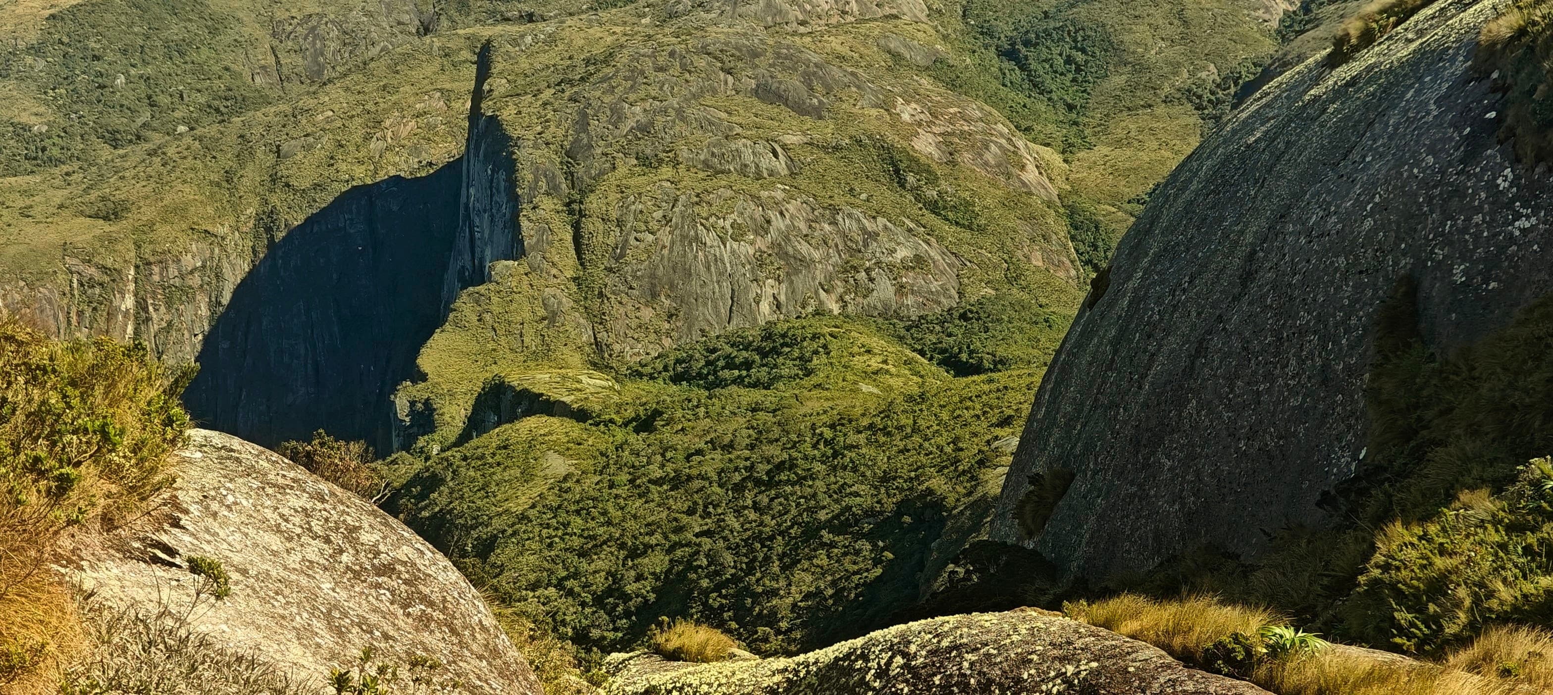 A deep green cleft between steep granite slabs with a narrow rock tower casting a shadow.