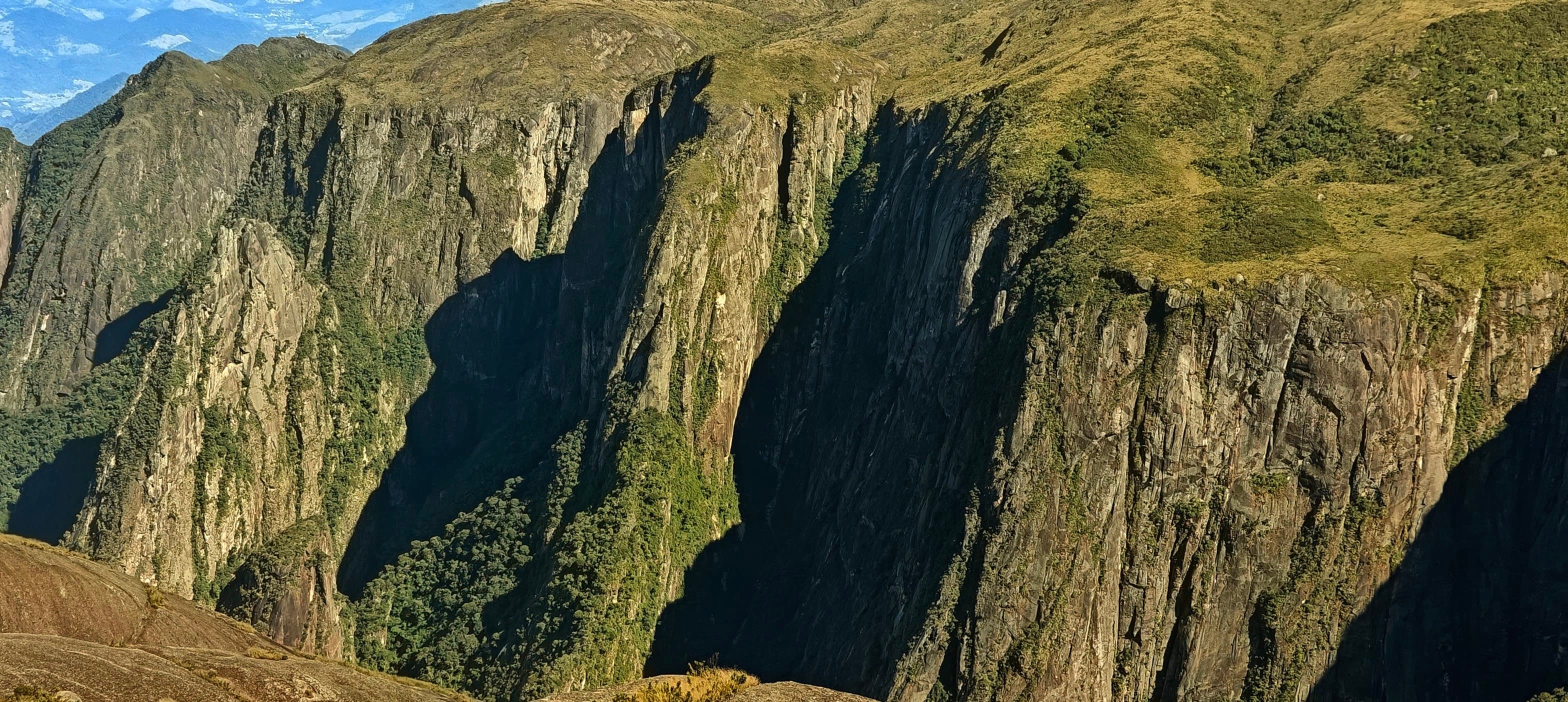 Tall vertical cliffs with deep shadows and vegetation clinging to ledges below the summit.