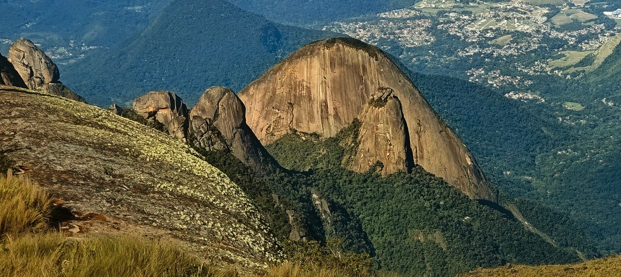 A large rounded granite dome rising above forested slopes with a city visible in the distance.