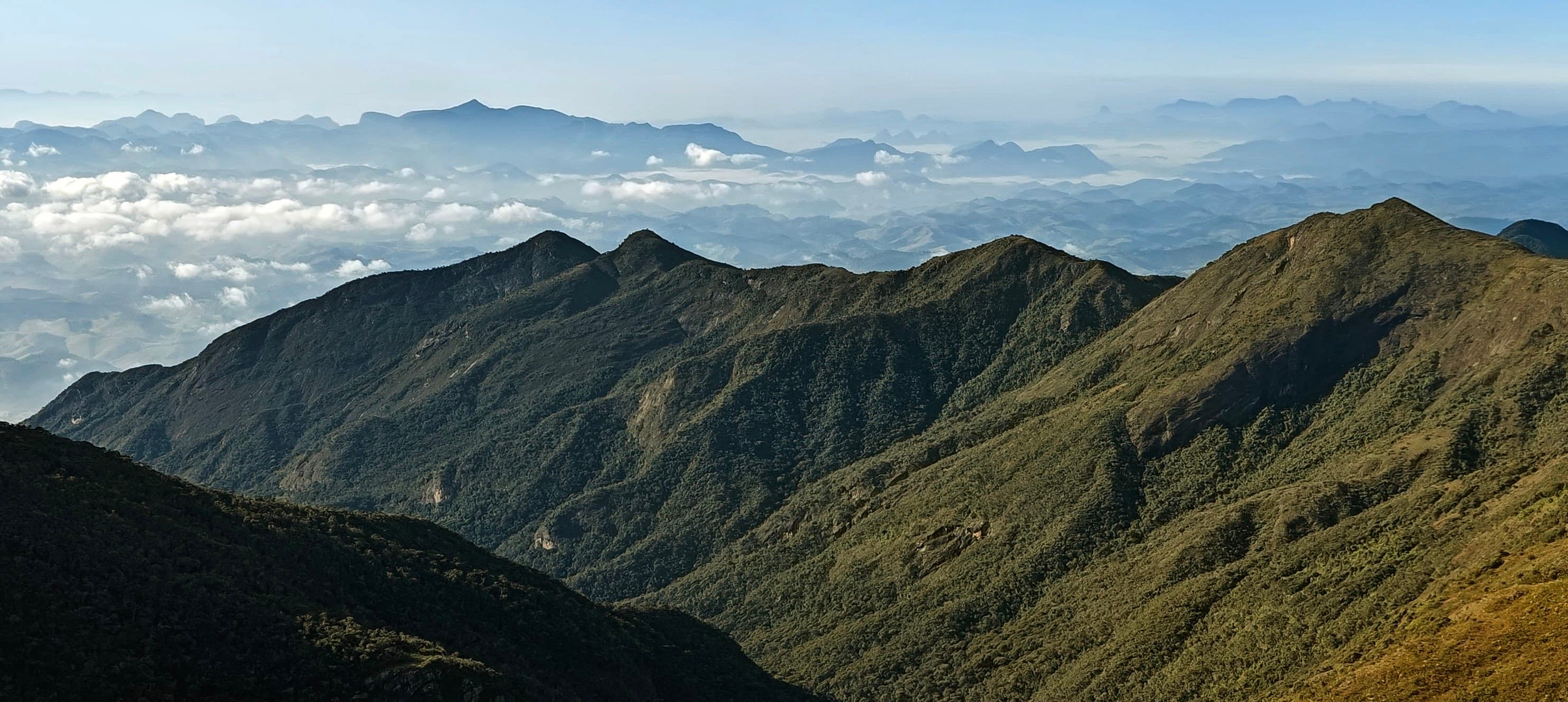 Green mountain ridges under a clear blue morning sky in the Caparaó massif.