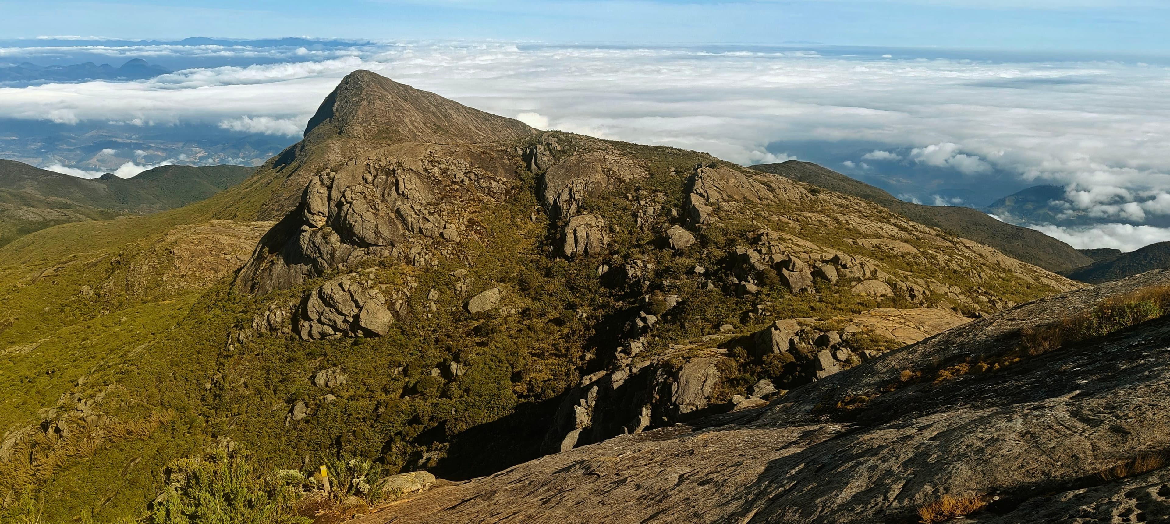 Rocky peak and high ridge rising above a bright layer of clouds in the Caparaó massif.