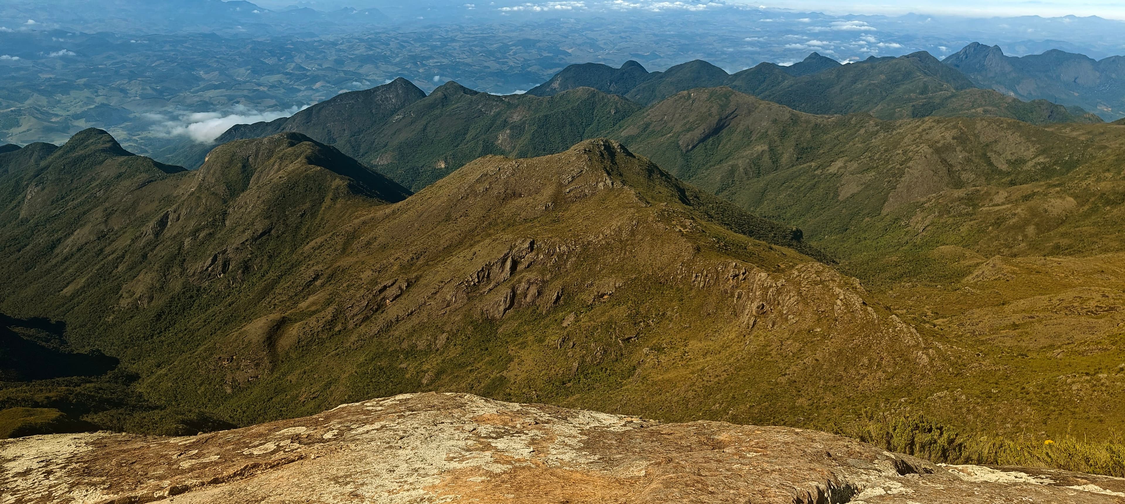 Deep green valleys and angular ridges seen from the rocky summit of Pico da Bandeira.