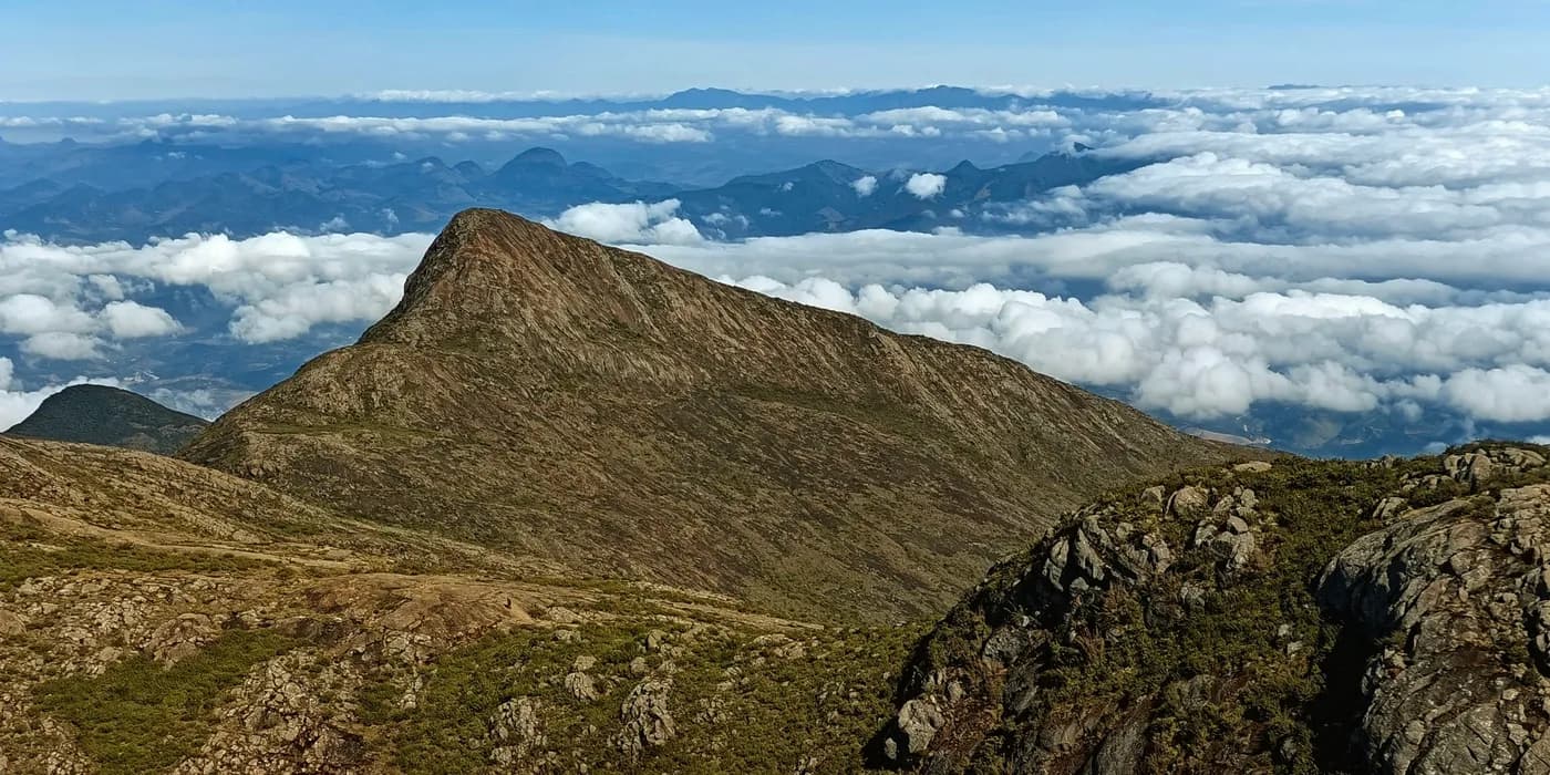 Rocky Caparaó ridge rising above a broad sea of clouds, seen from Pico da Bandeira.