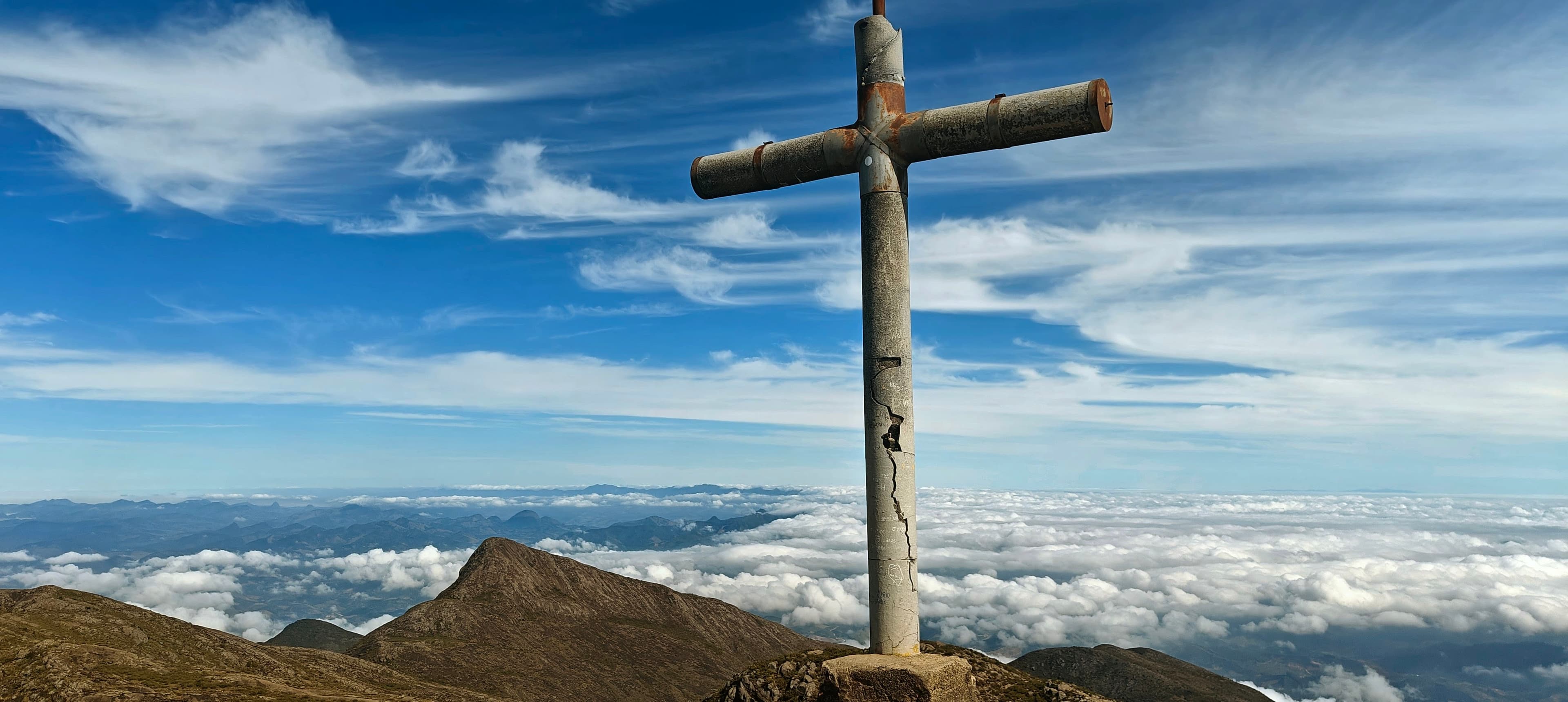 Tall summit cross on Pico da Bandeira above neighboring ridges and a sea of clouds.