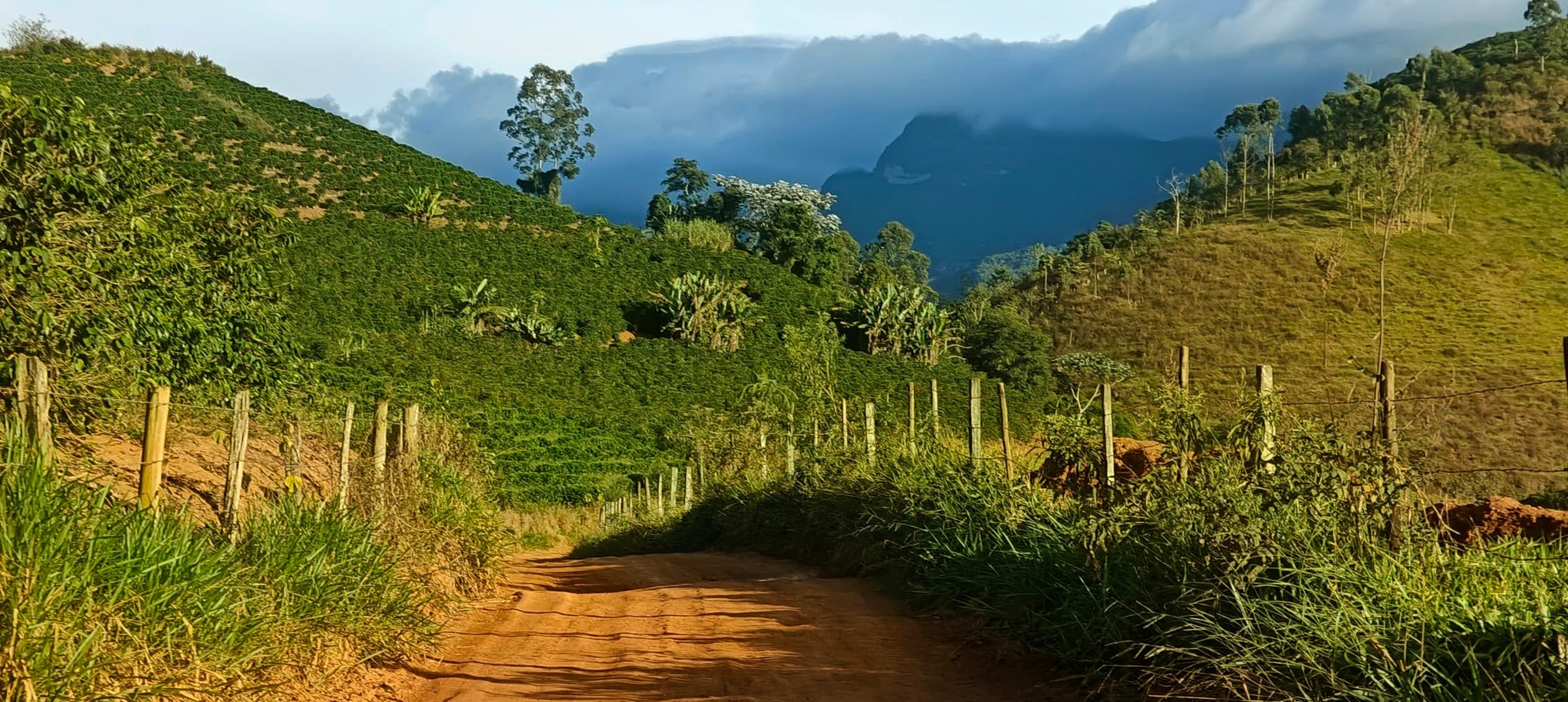 Red dirt road running between green slopes towards cloud-covered mountains.