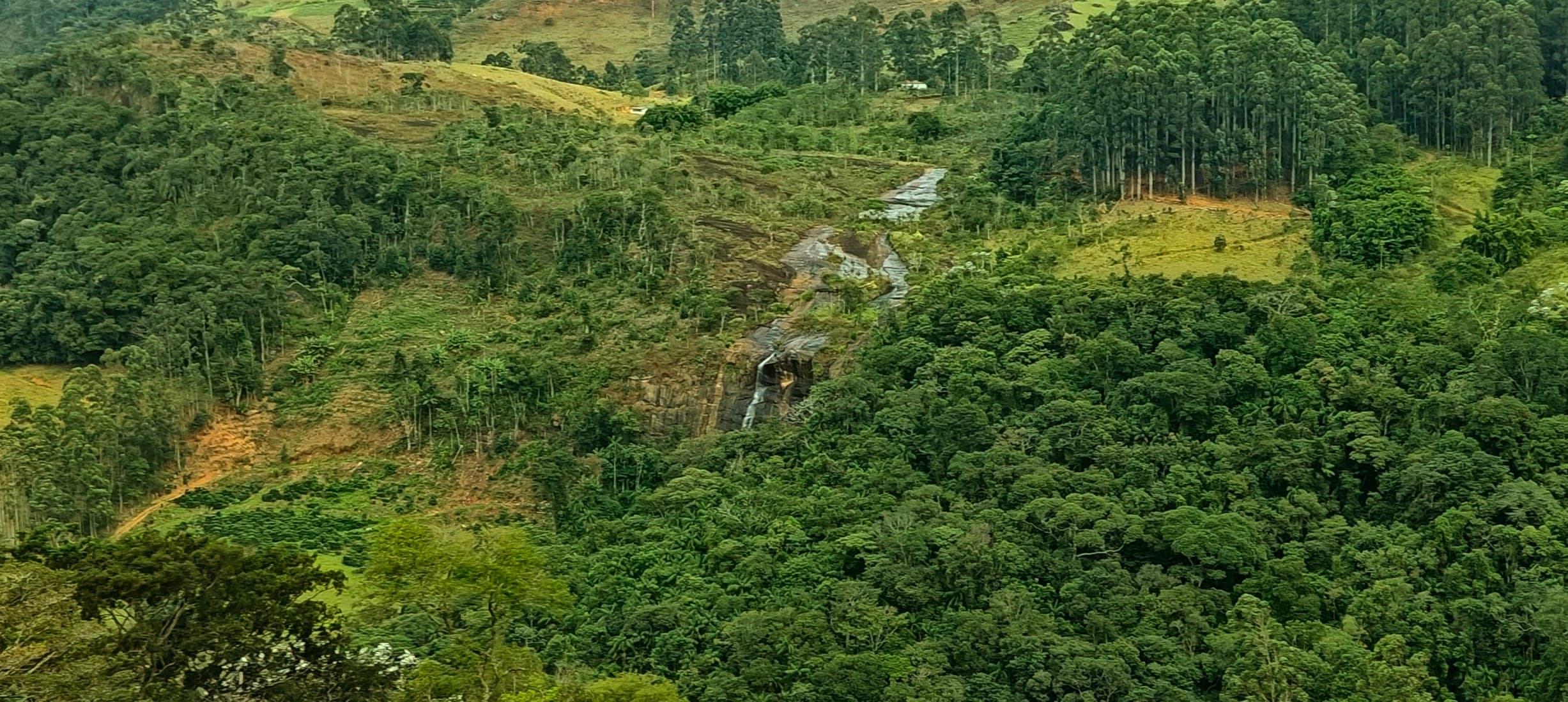 Narrow waterfall descending through a green valley on the far slope.