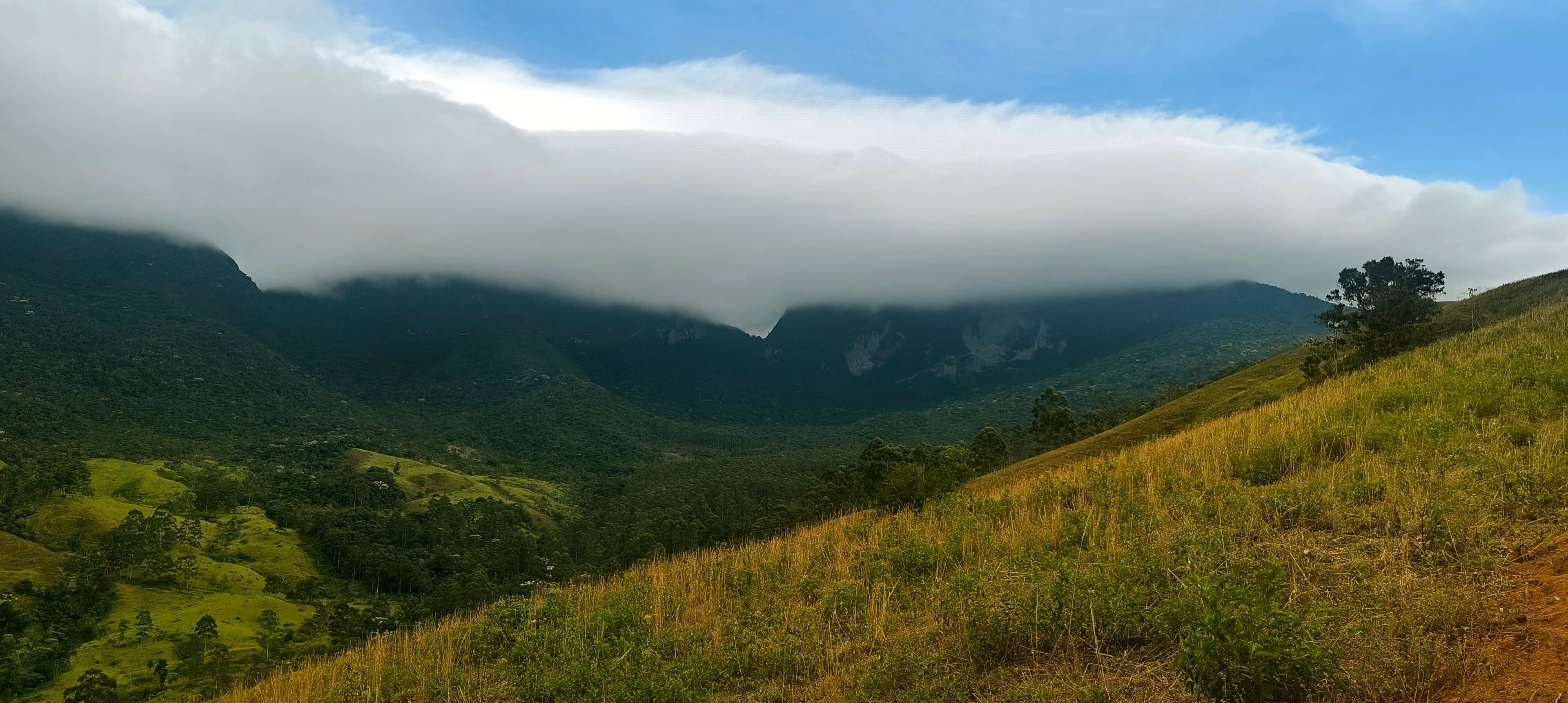 Low white cloud spilling over a dark mountain ridge above a green valley.