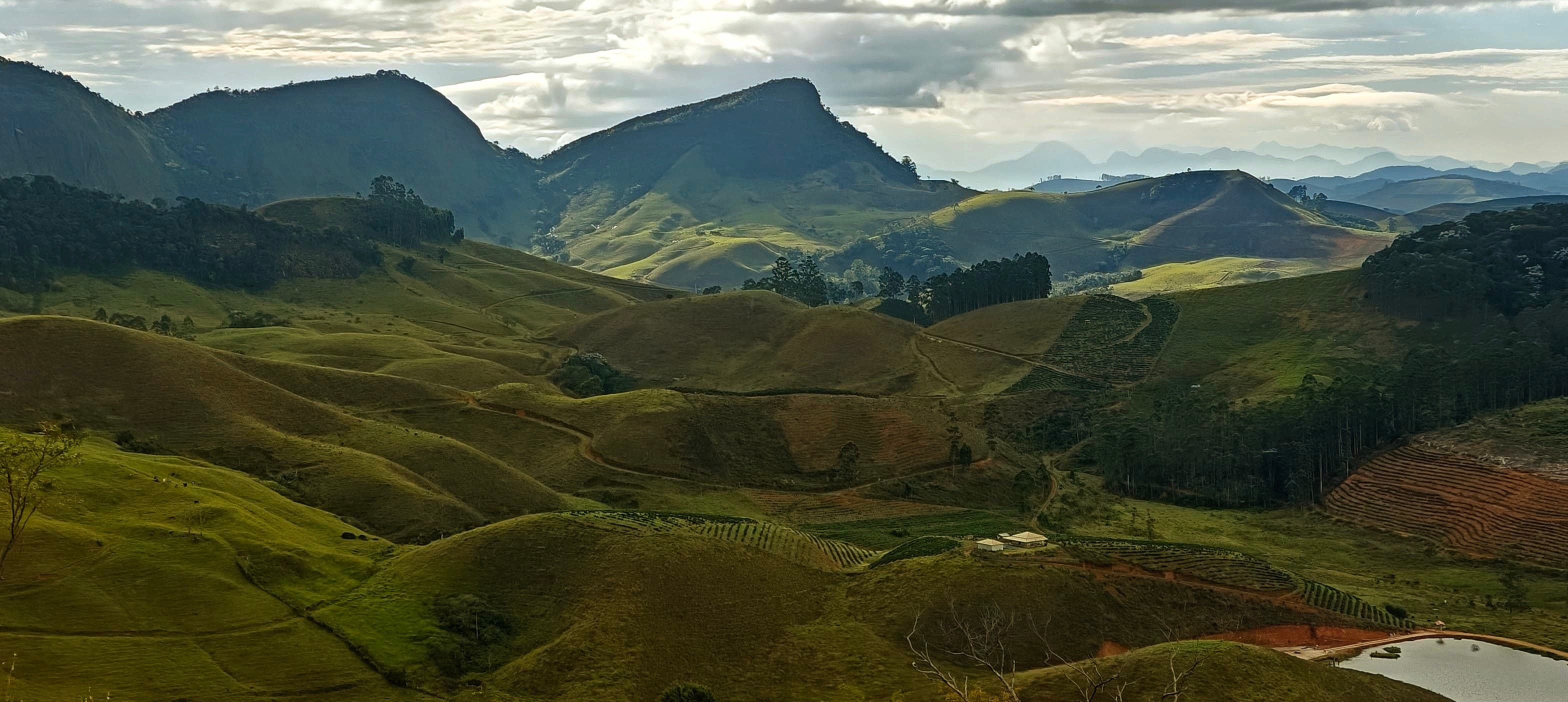 Rounded green hills leading towards dark mountain ridges under broken cloud.