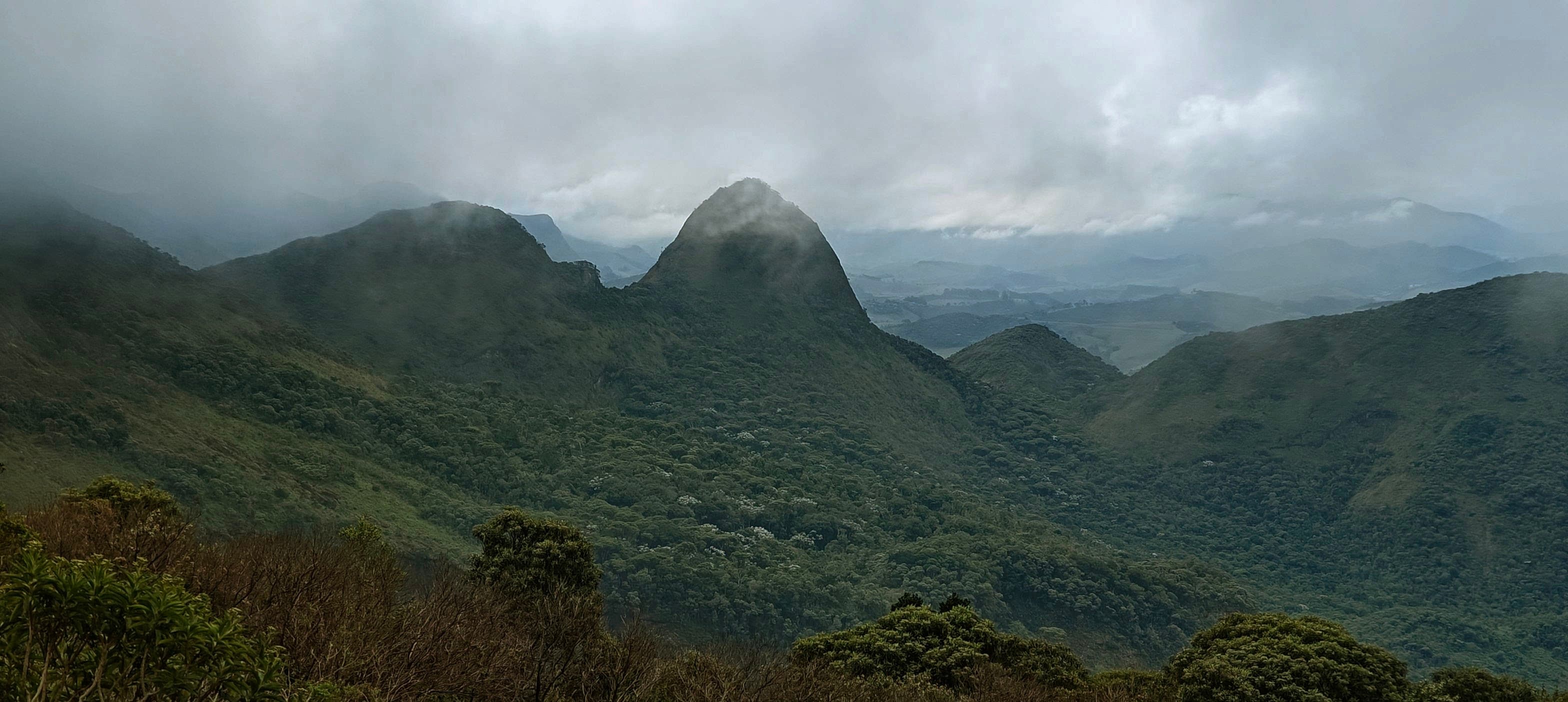 Low cloud wrapping dark twin mountain summits above a deep forested valley.