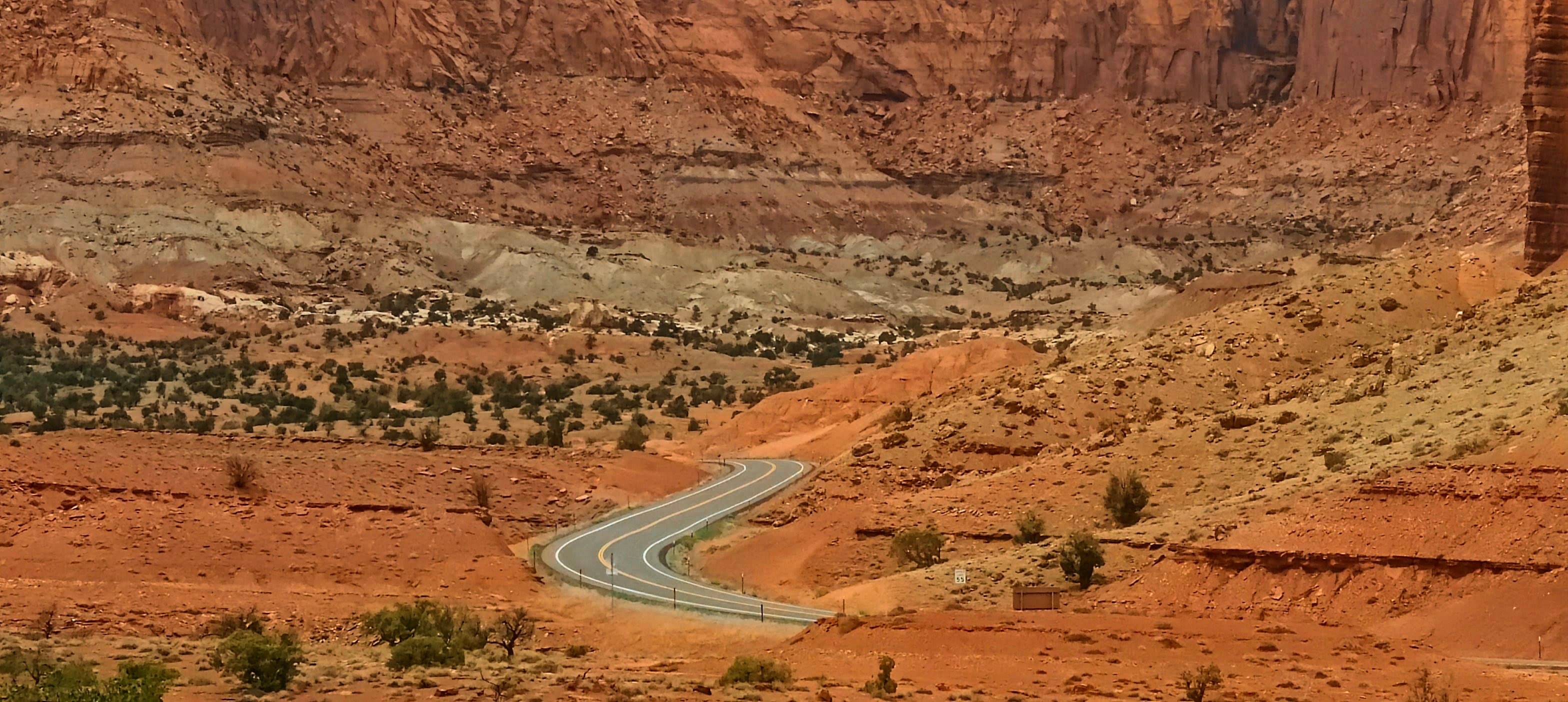 A paved road curving through a broad red-rock desert basin beneath layered cliffs in Capitol Reef National Park.