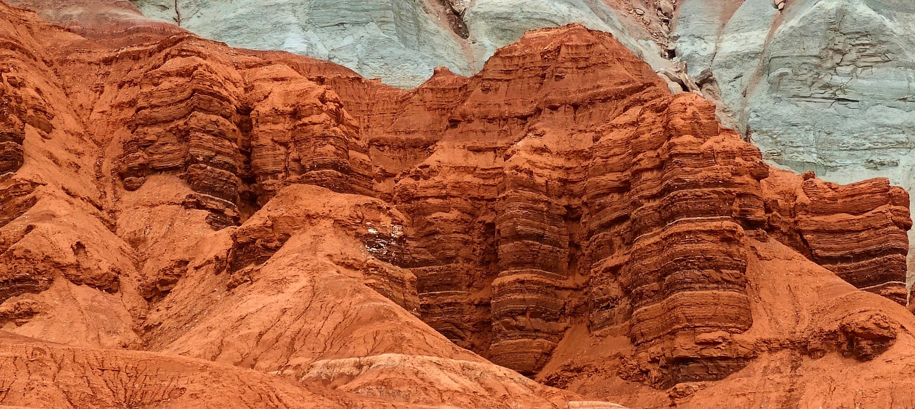 Rounded and deeply eroded red rock layers beneath a pale cliff in Capitol Reef National Park.