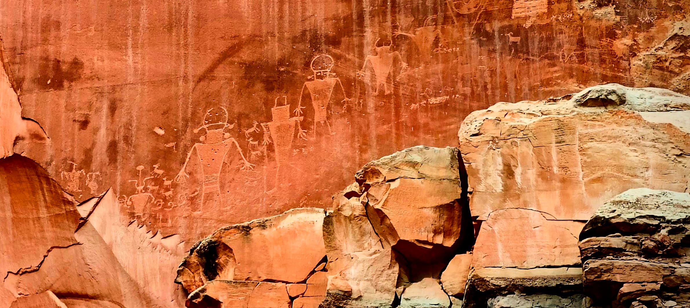 Fremont Culture petroglyph figures visible on a red sandstone wall above broken boulders in Capitol Reef National Park.