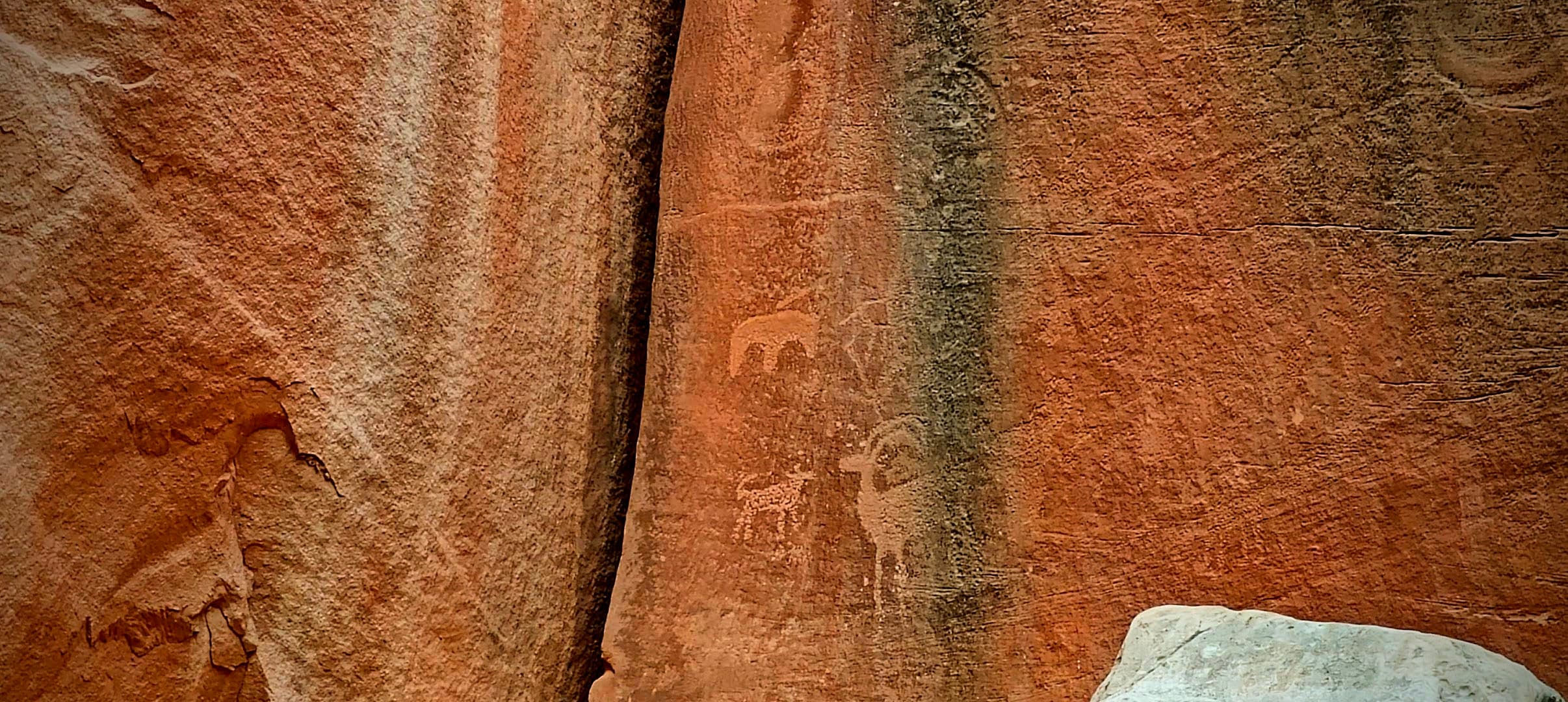 Faint Fremont Culture petroglyph figures visible in darker desert varnish along a narrow sandstone seam.