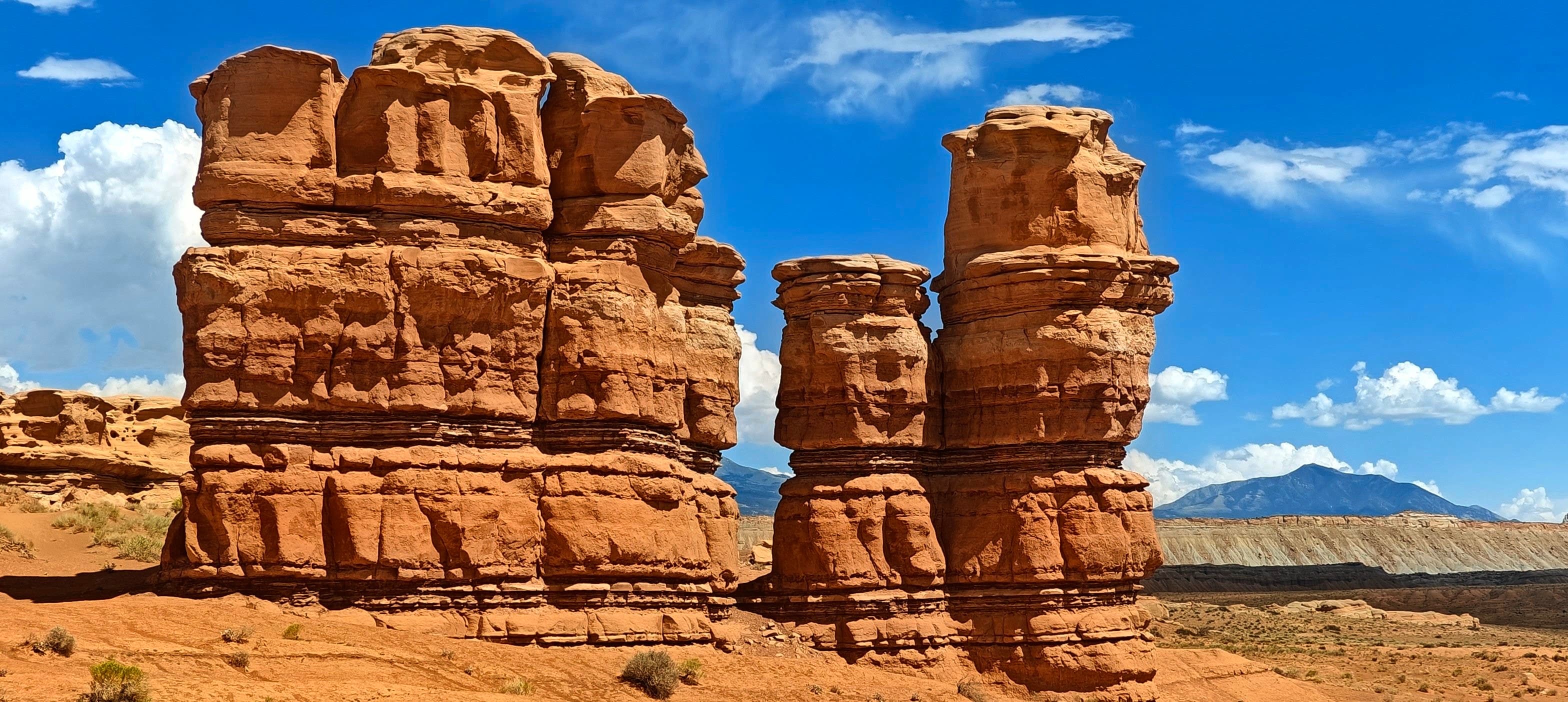 Massive freestanding red sandstone towers rising against a vivid blue sky with white clouds east of Capitol Reef.