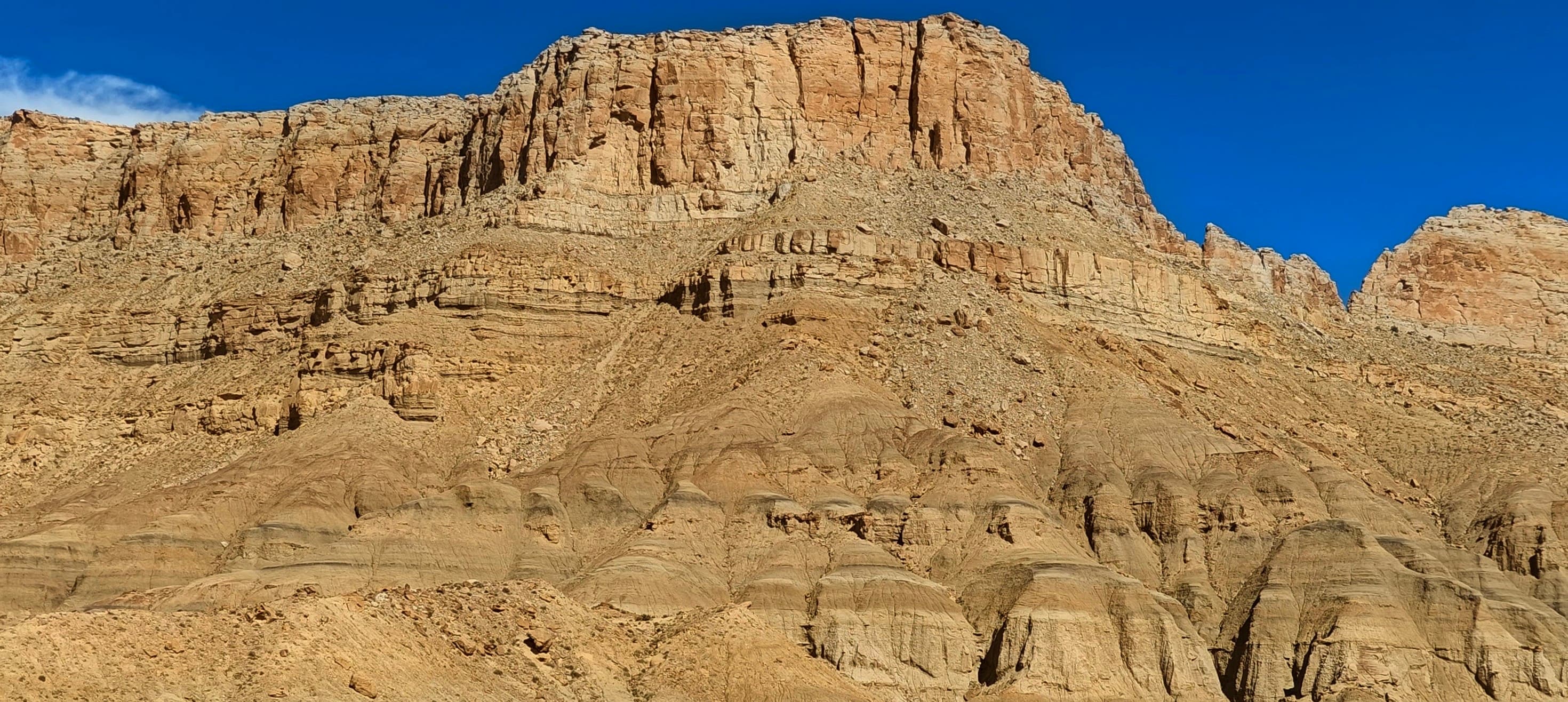 A broad pale tan cliff with layered rock and eroded lower slopes in the desert east of Capitol Reef.