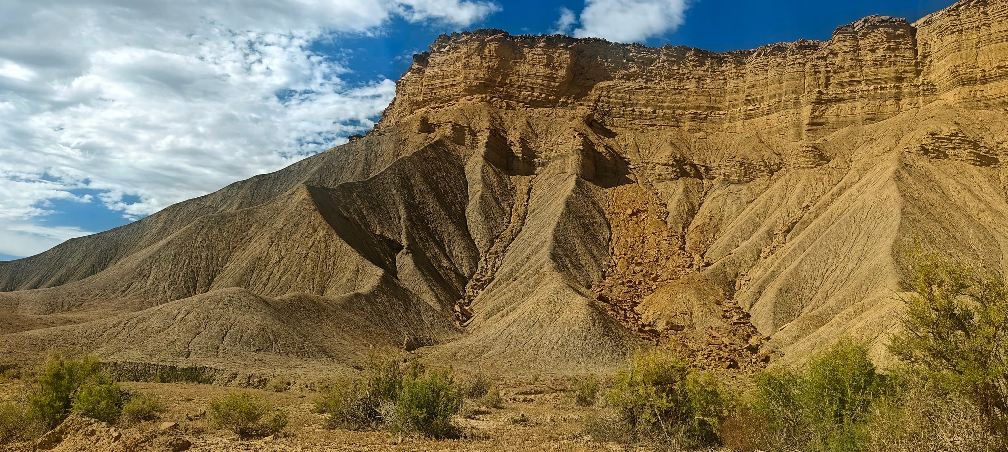 Steep gray-tan badland slopes cut by deep gullies beneath a high layered ridge near Caineville, Utah.