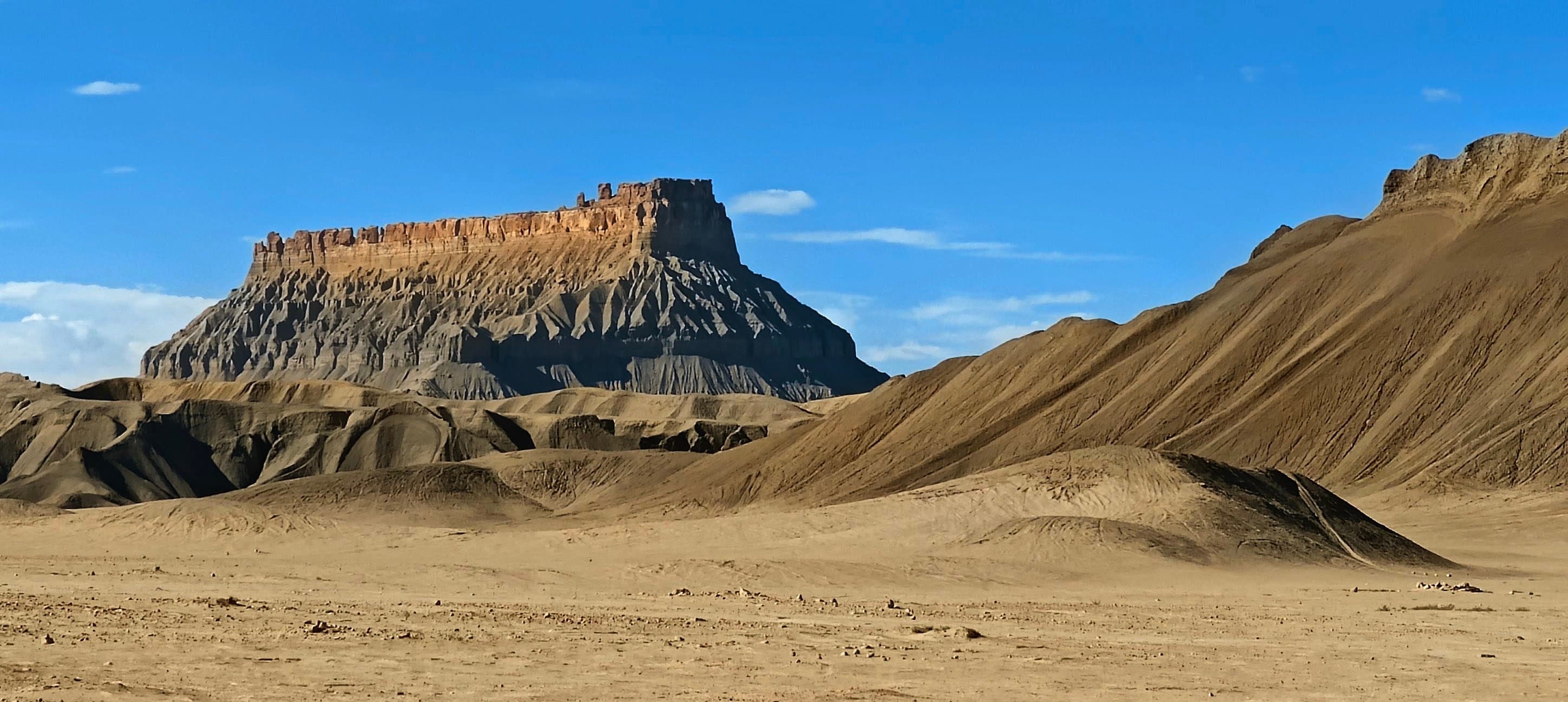 A flat-topped butte framed by smooth gray-brown badland ridges in the Factory Butte area of Utah.