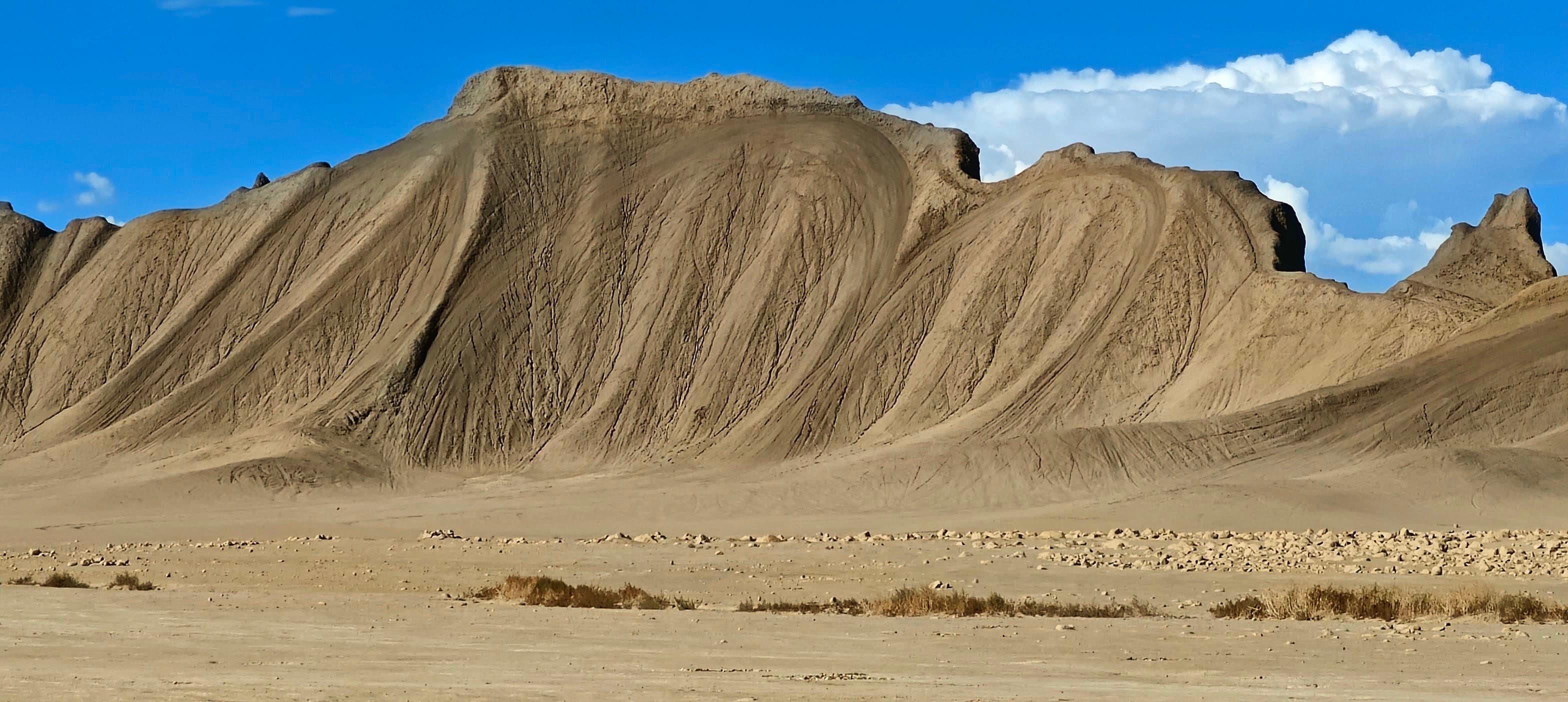 A long gray-brown badland ridge etched with closely spaced erosion lines above a flat desert plain.