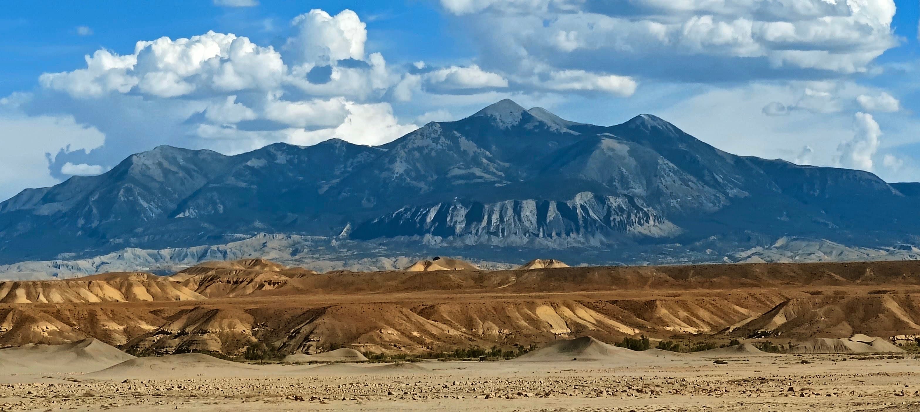A dark mountain range beneath cumulus clouds beyond layered tan and gray badlands in central Utah.