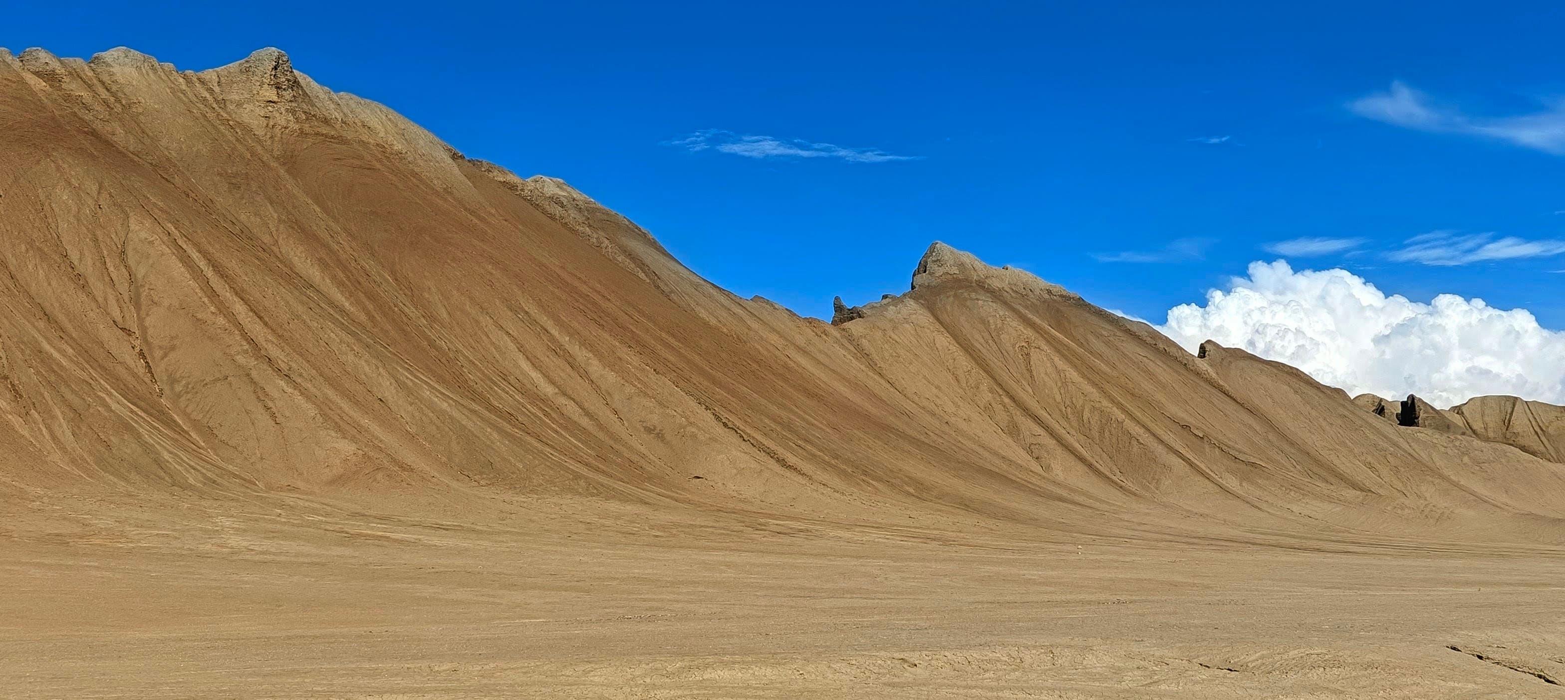 A long smooth tan badland ridge with fine erosion lines beneath a saturated blue sky.