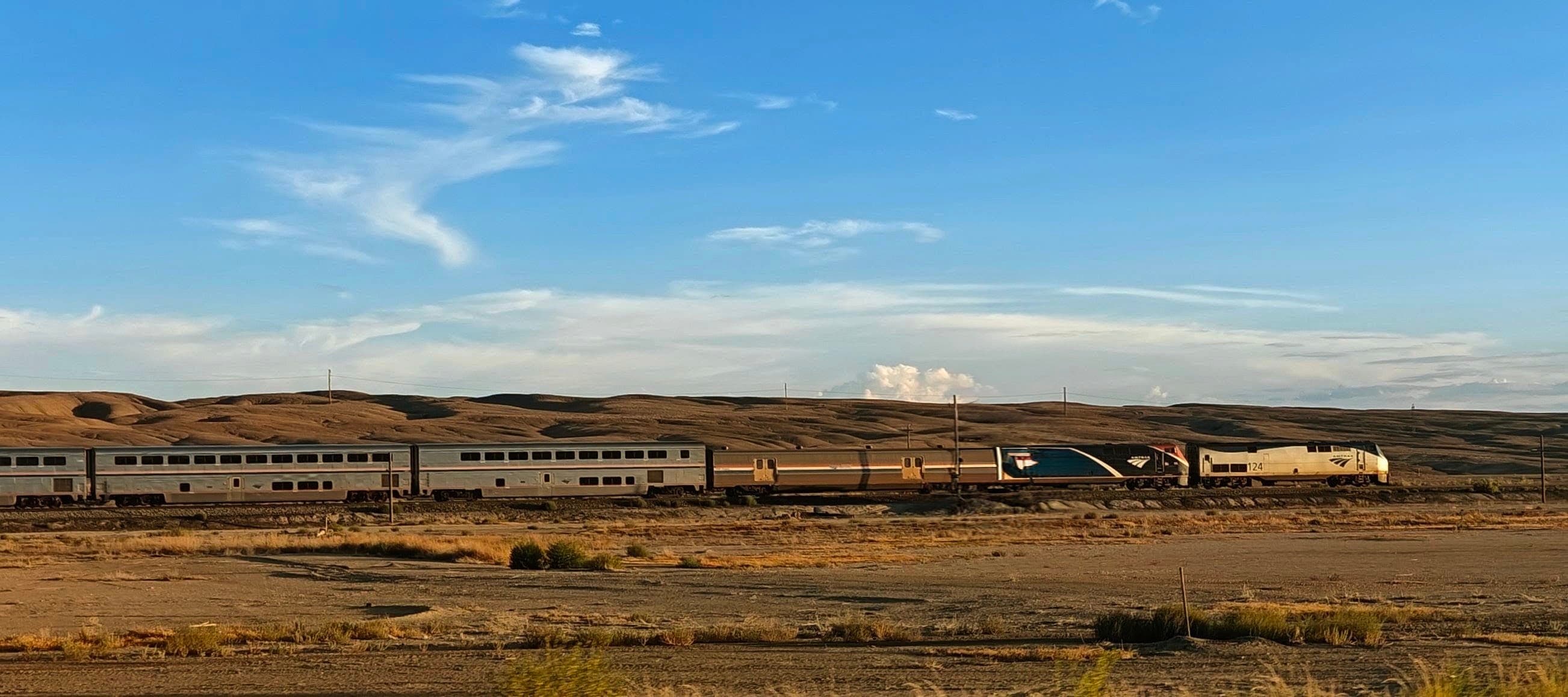 A long passenger train crossing an open, sparsely vegetated Utah desert beneath a wide blue sky.