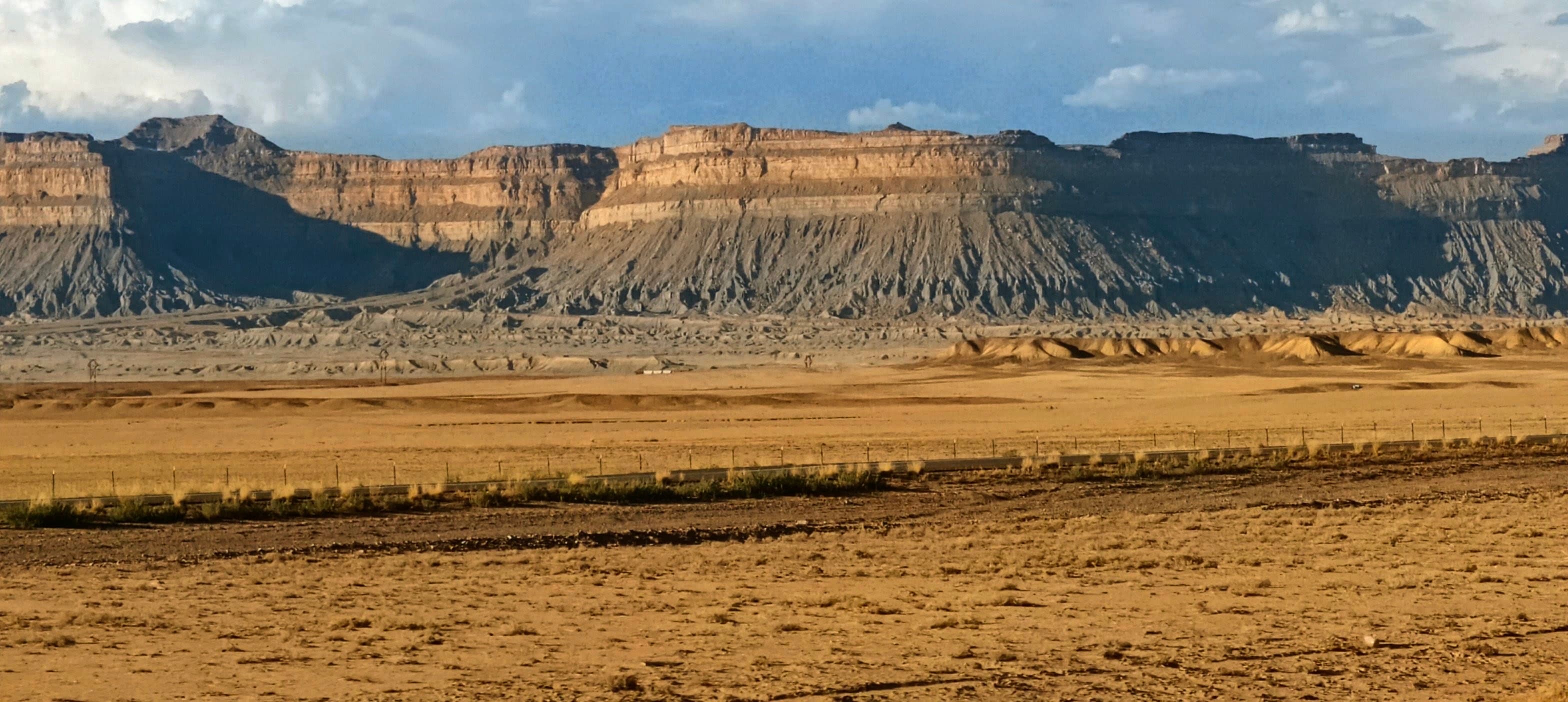 A broad flat-topped mesa stretching across an open desert plain beneath broken clouds in central Utah.