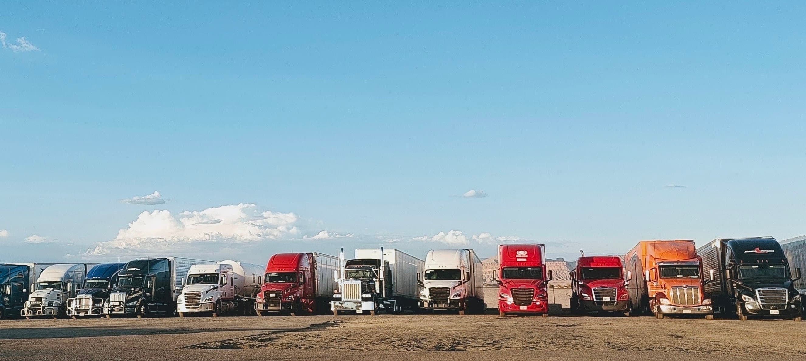 A line of parked semi-trucks and trailers beneath a wide pale-blue sky in the open Utah desert.