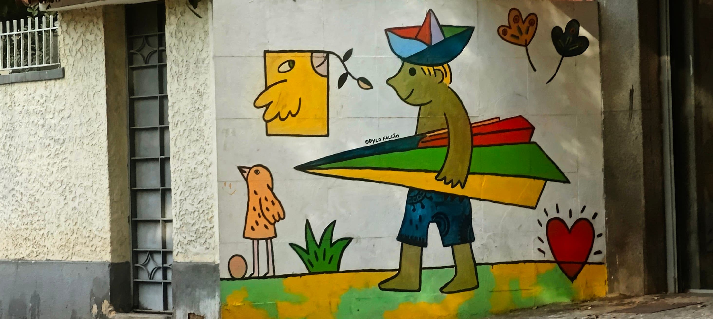 A colourful cartoon figure carrying a long board is painted on a pale wall.