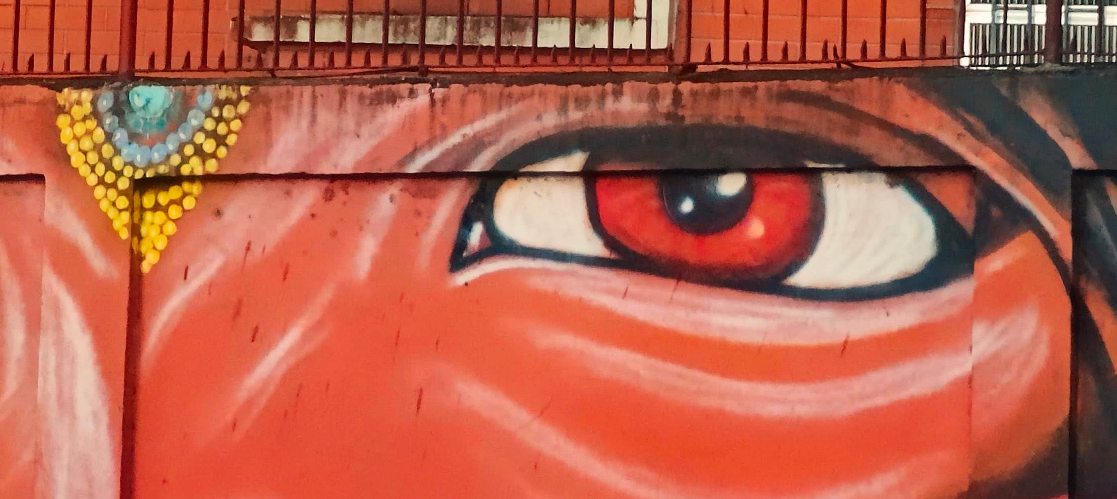 A large red painted eye fills a wall behind a horizontal metal railing.