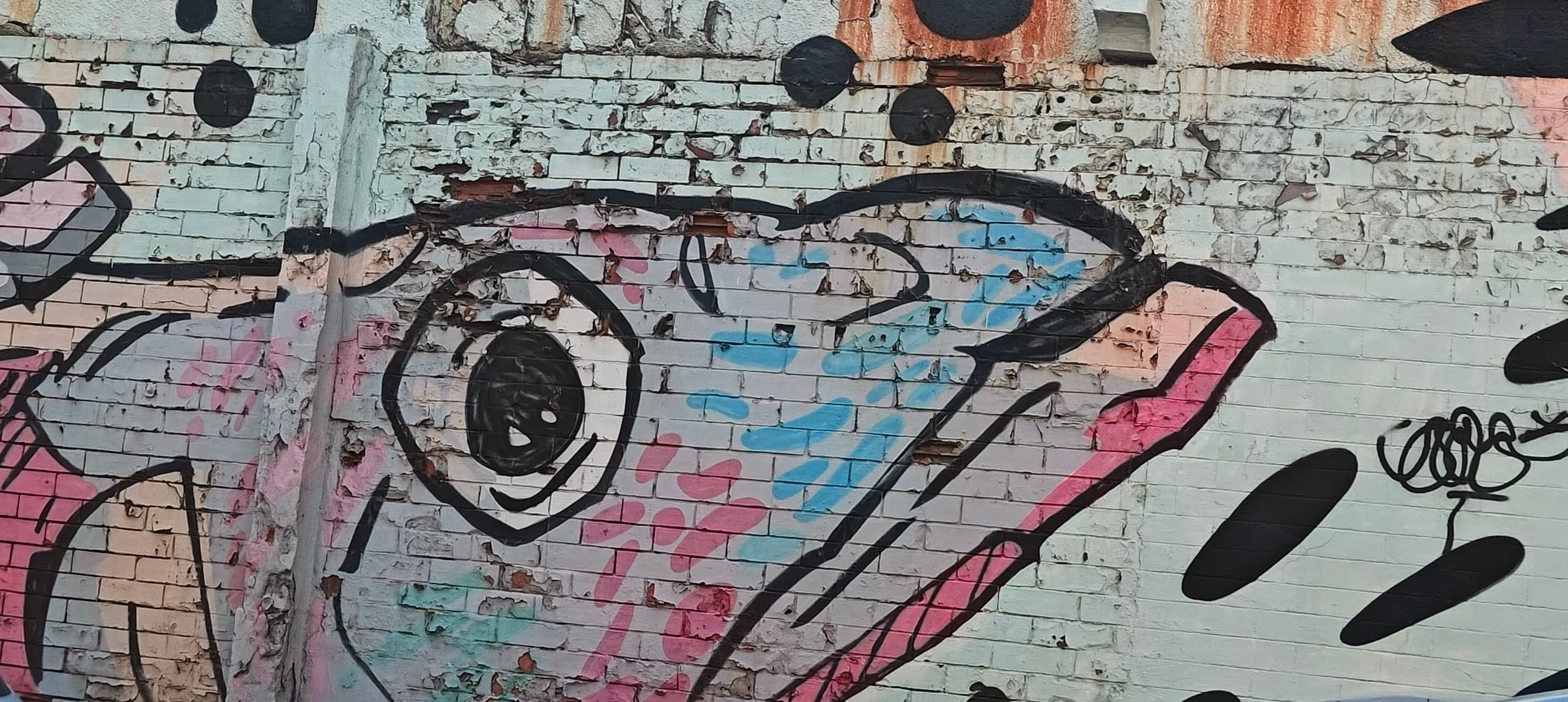 An abstract black-and-white eye is painted over exposed brick and layered graffiti.