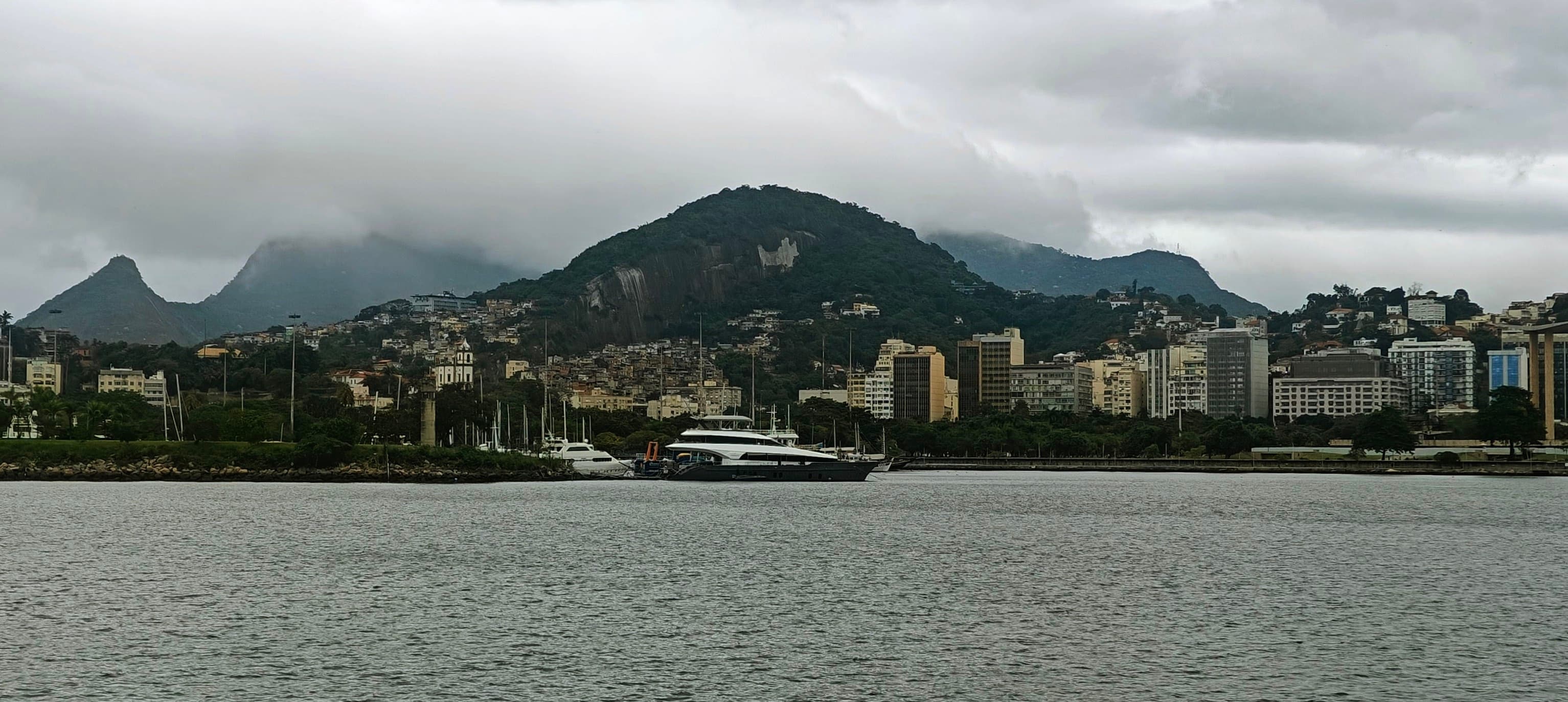 Rio’s green hills and dense neighbourhoods rise across calm water beneath low cloud.
