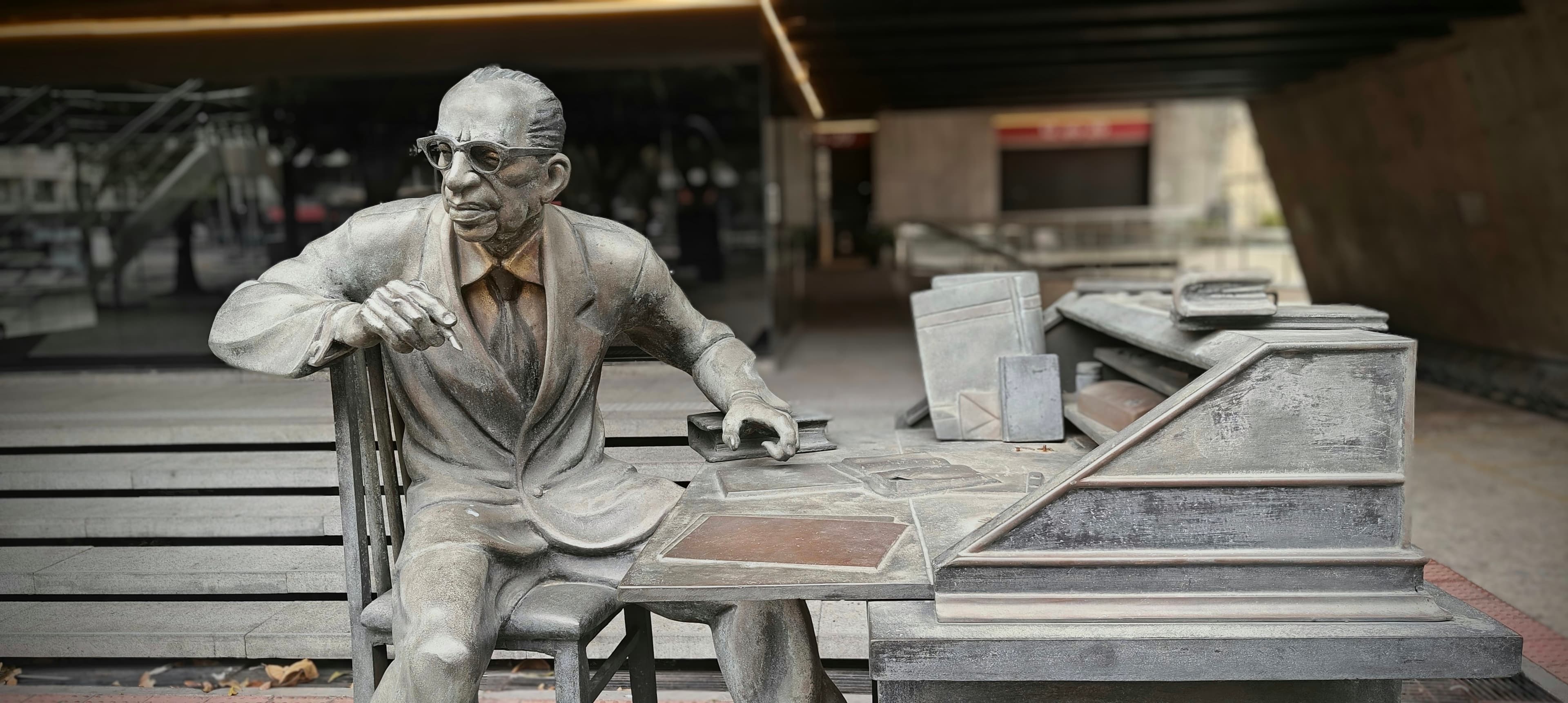 A bronze statue depicts Manuel Bandeira seated at a desk with books and papers.
